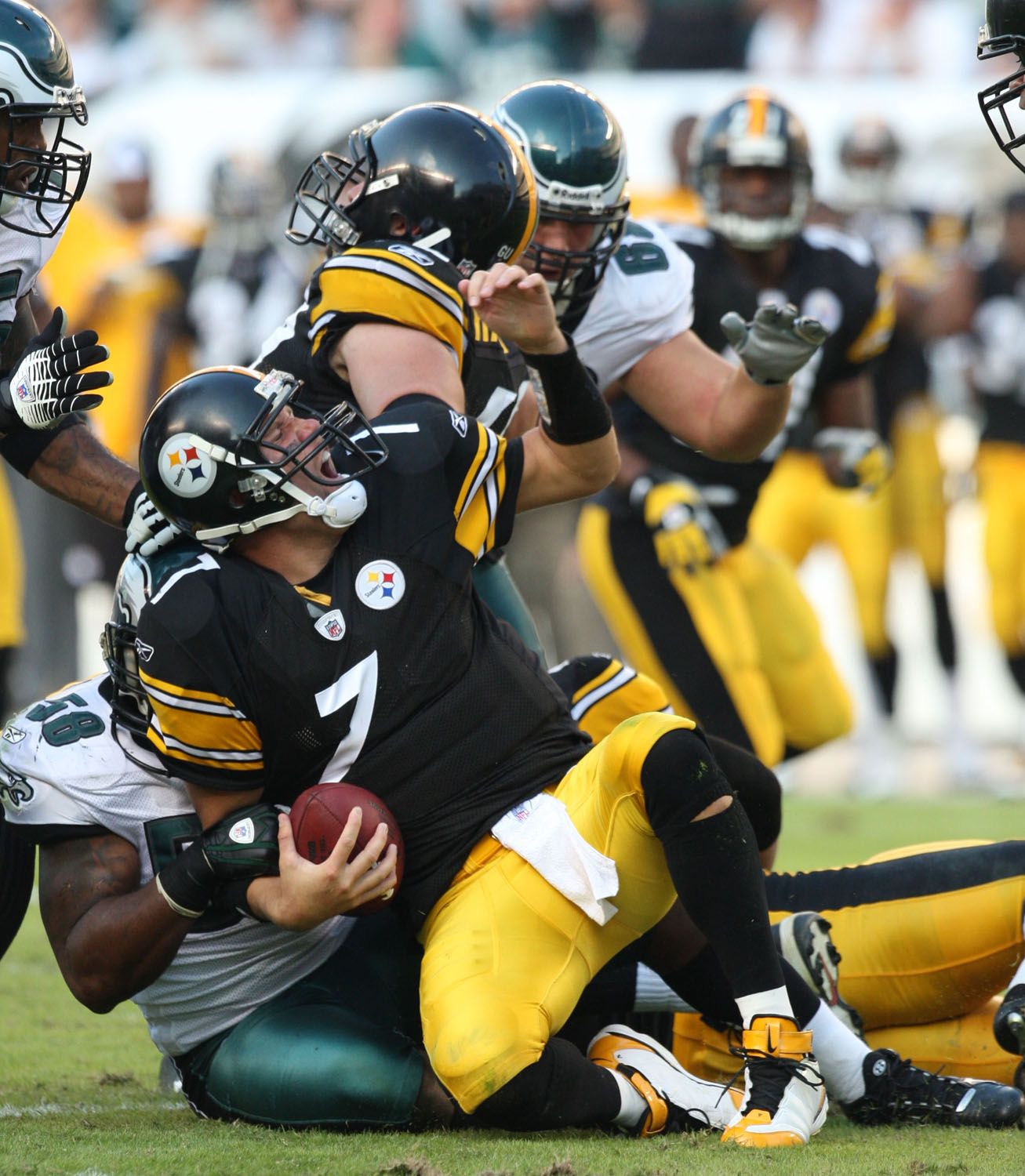 Steelers quarterback in black jersey gets tackled by Eagles defenders during NFL game.