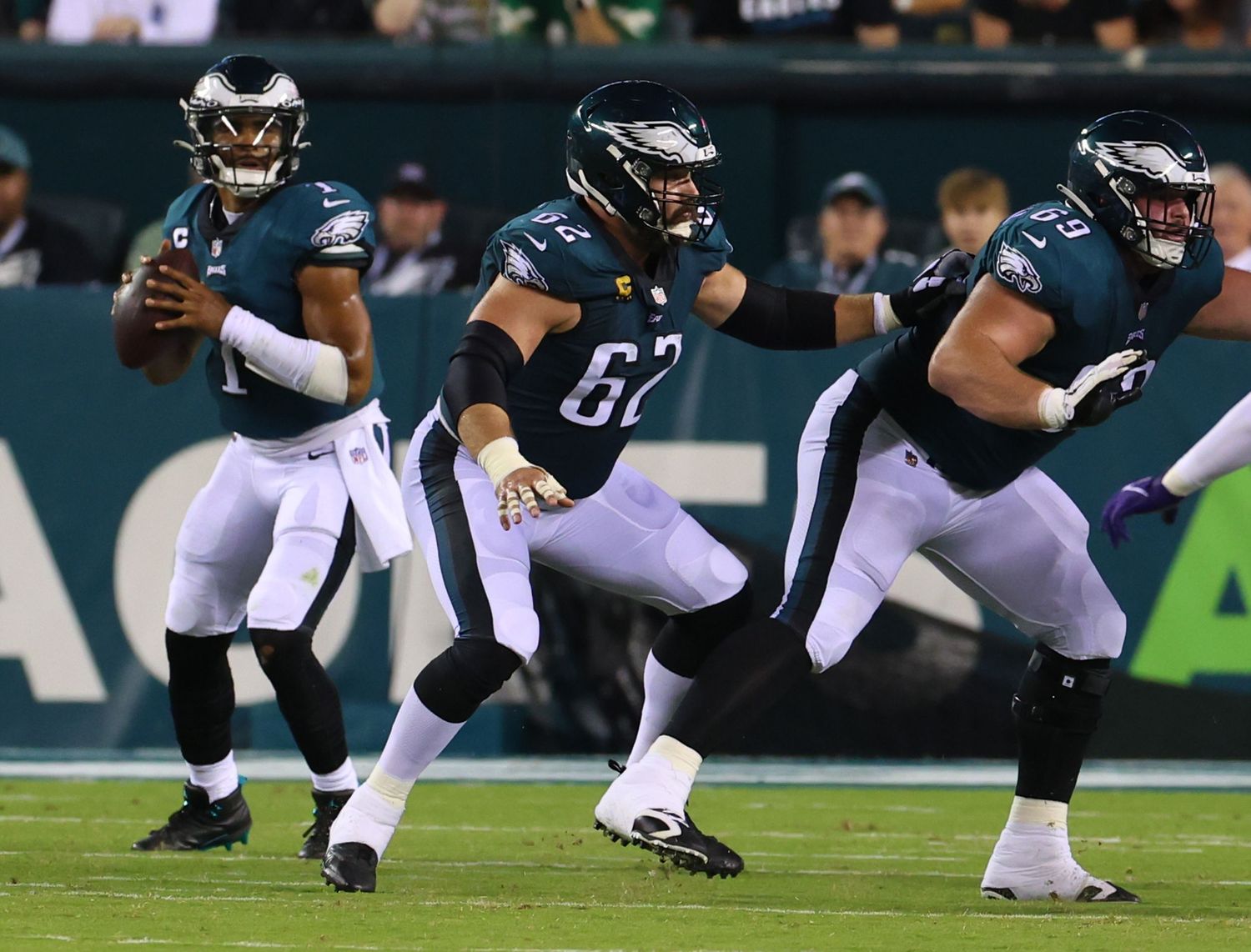 Football players in dark uniforms lined up on field during game action.
