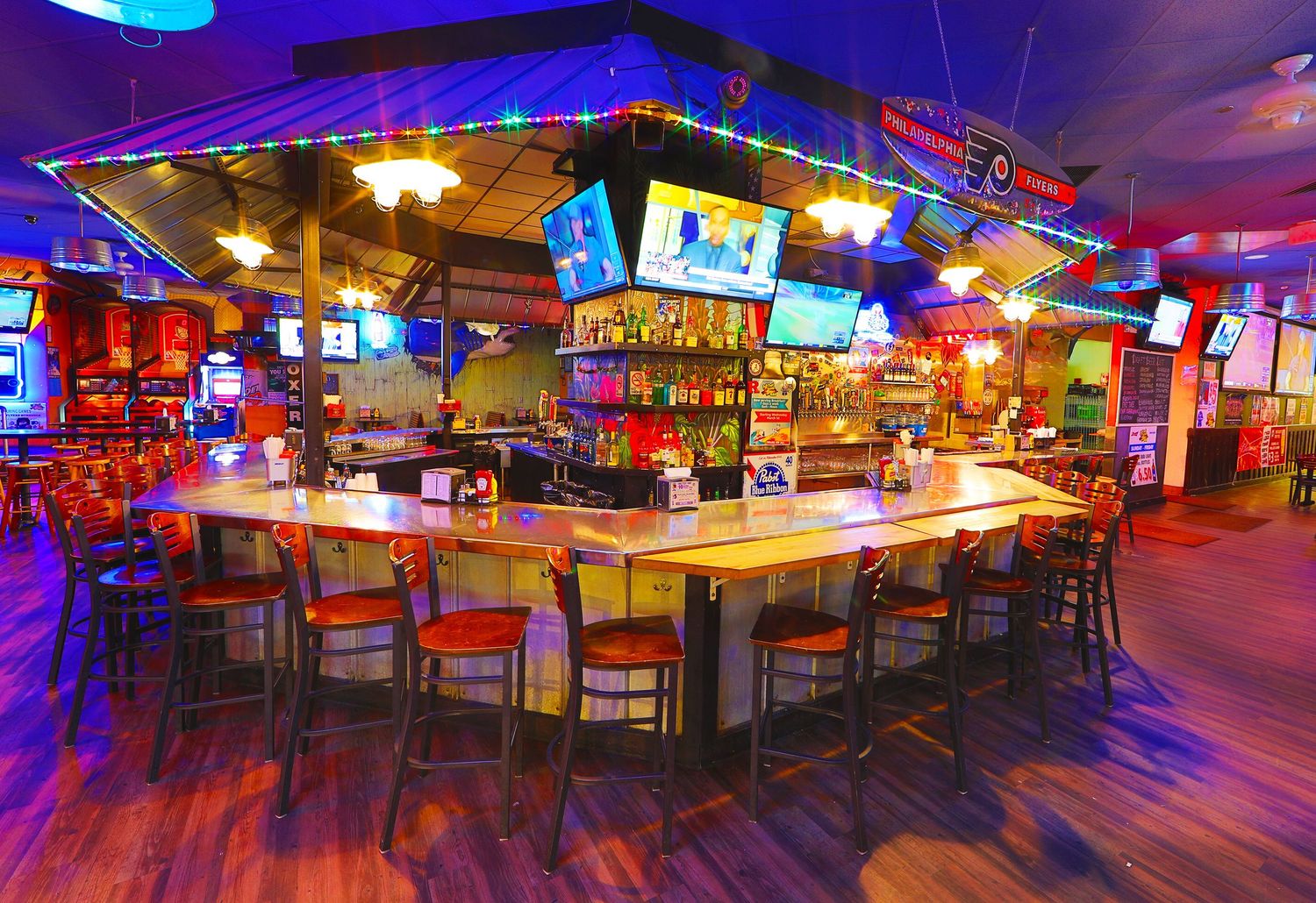Panoramic view of a dimly lit bar with red and blue accent lighting and wooden floors.