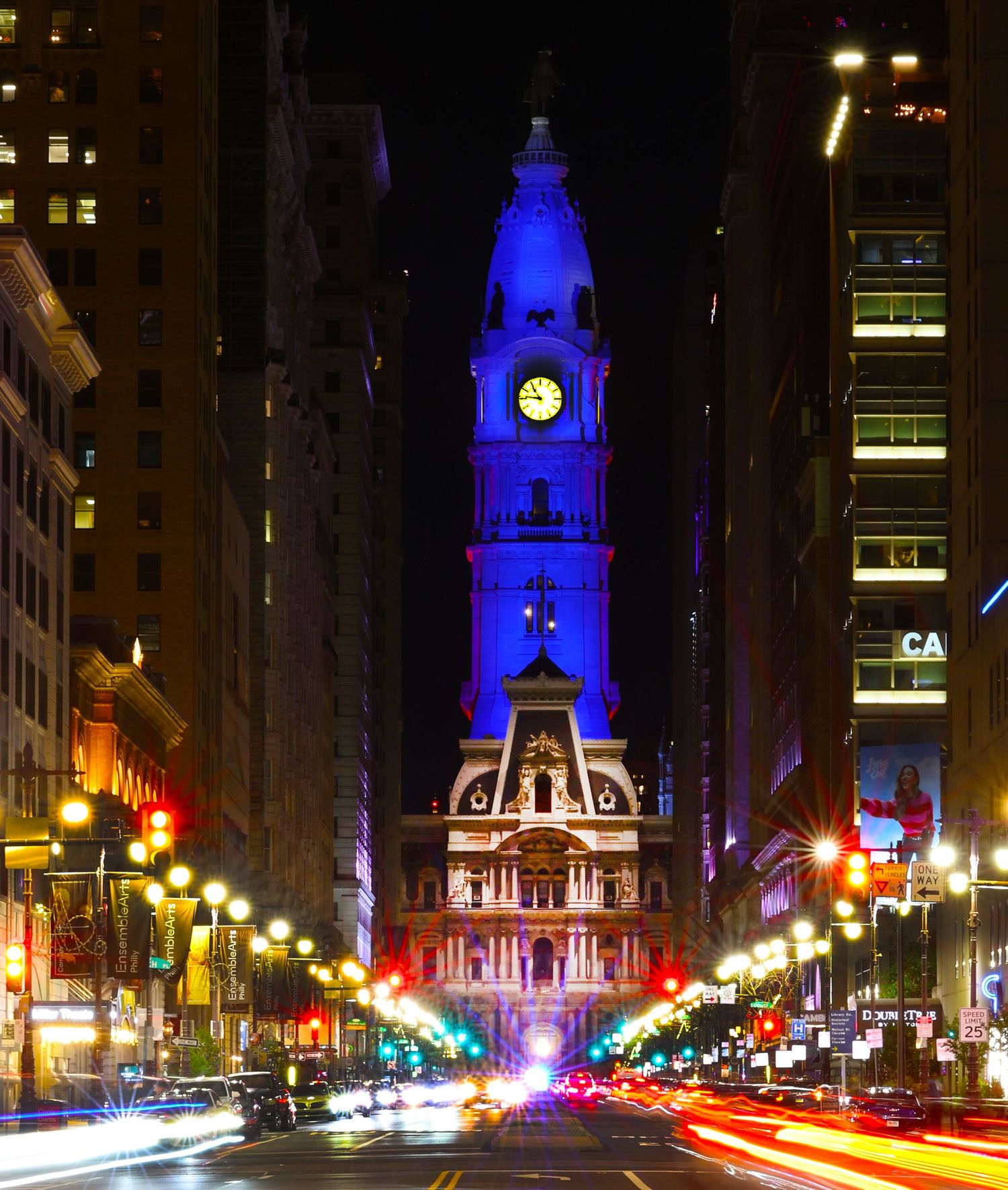 Philadelphia city hall lit in blue at night with light trails from traffic.