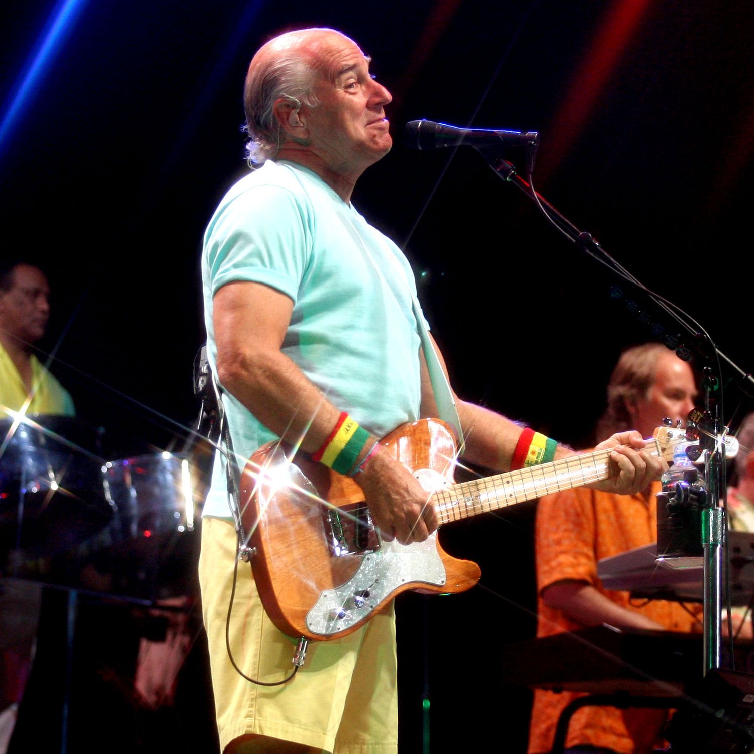 Band members playing guitars and instruments under blue and red stage lighting.