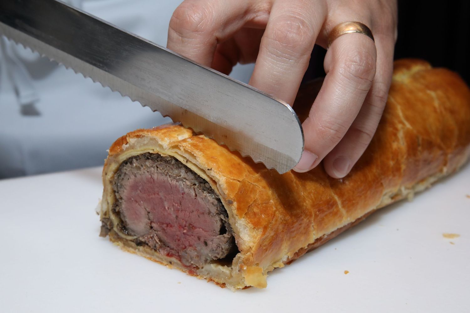 Slicing into golden brown beef wellington pastry revealing medium rare center.