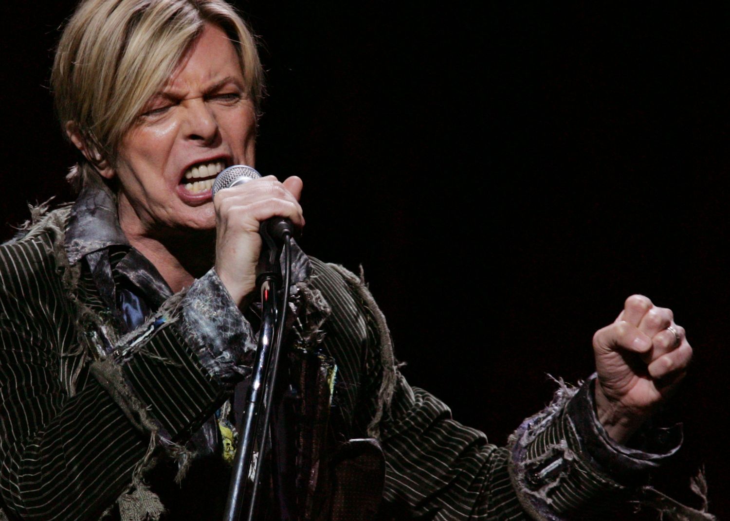 Performer singing passionately on stage against a dark background.
