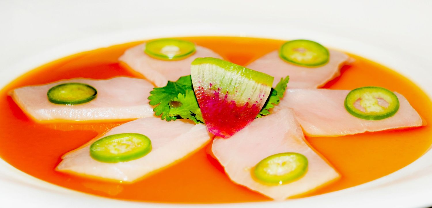 Colorful soup garnished with sliced jalapenos and herbs in vibrant orange broth.