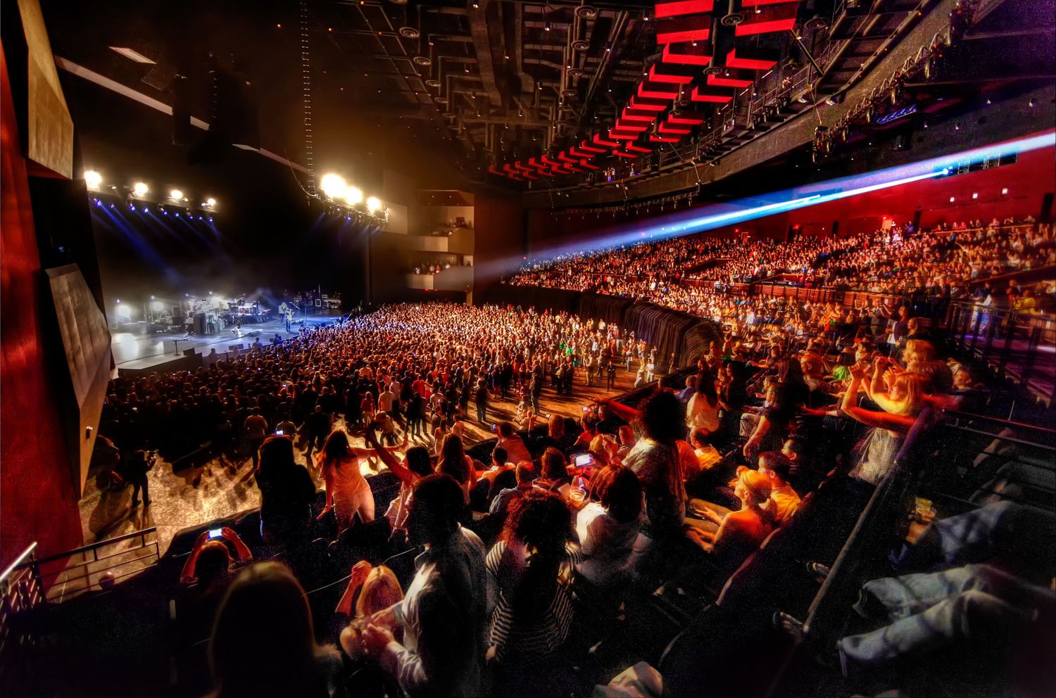 Large concert arena filled with spectators under dramatic red and blue lighting.