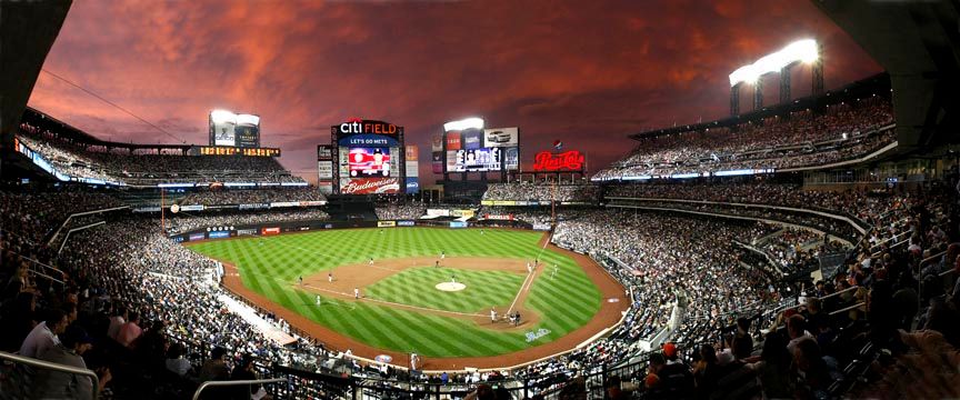 Panoramic view of a baseball stadium at sunset with crowd filling the stands.
