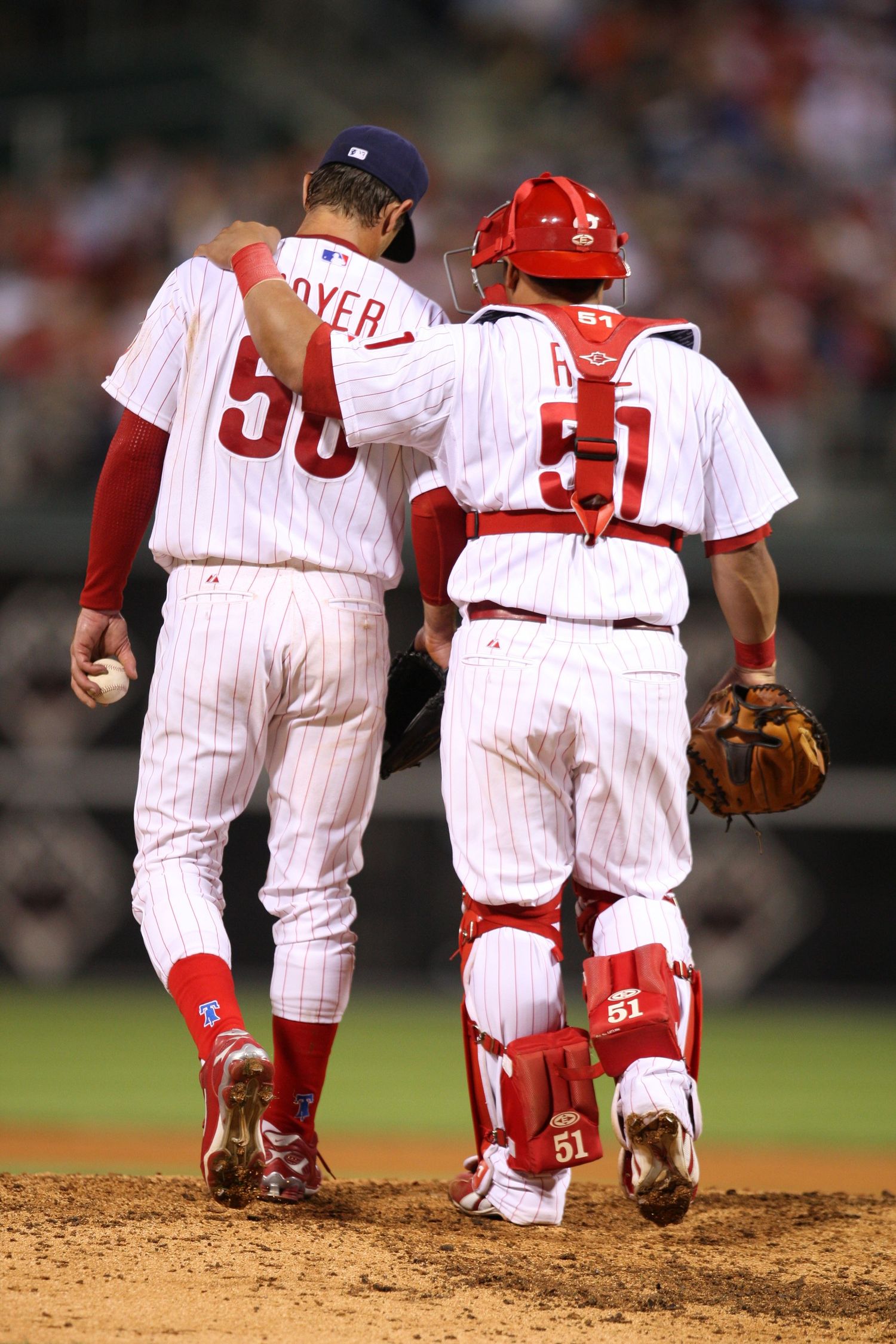 Baseball pitcher and catcher meet on mound wearing white pinstriped uniforms with red accents.