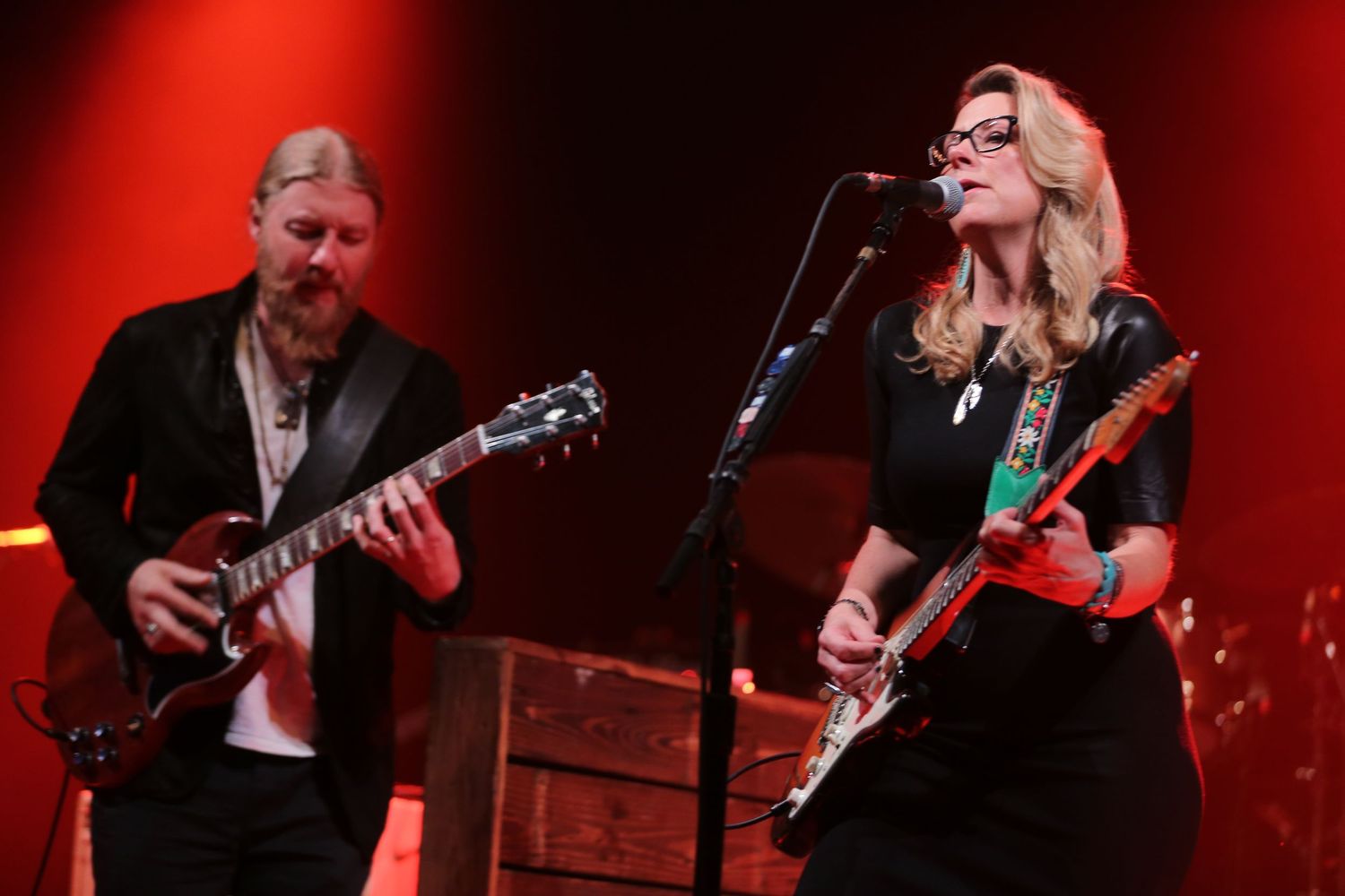 Musicians performing on stage with red dramatic lighting and guitar instrumentation.