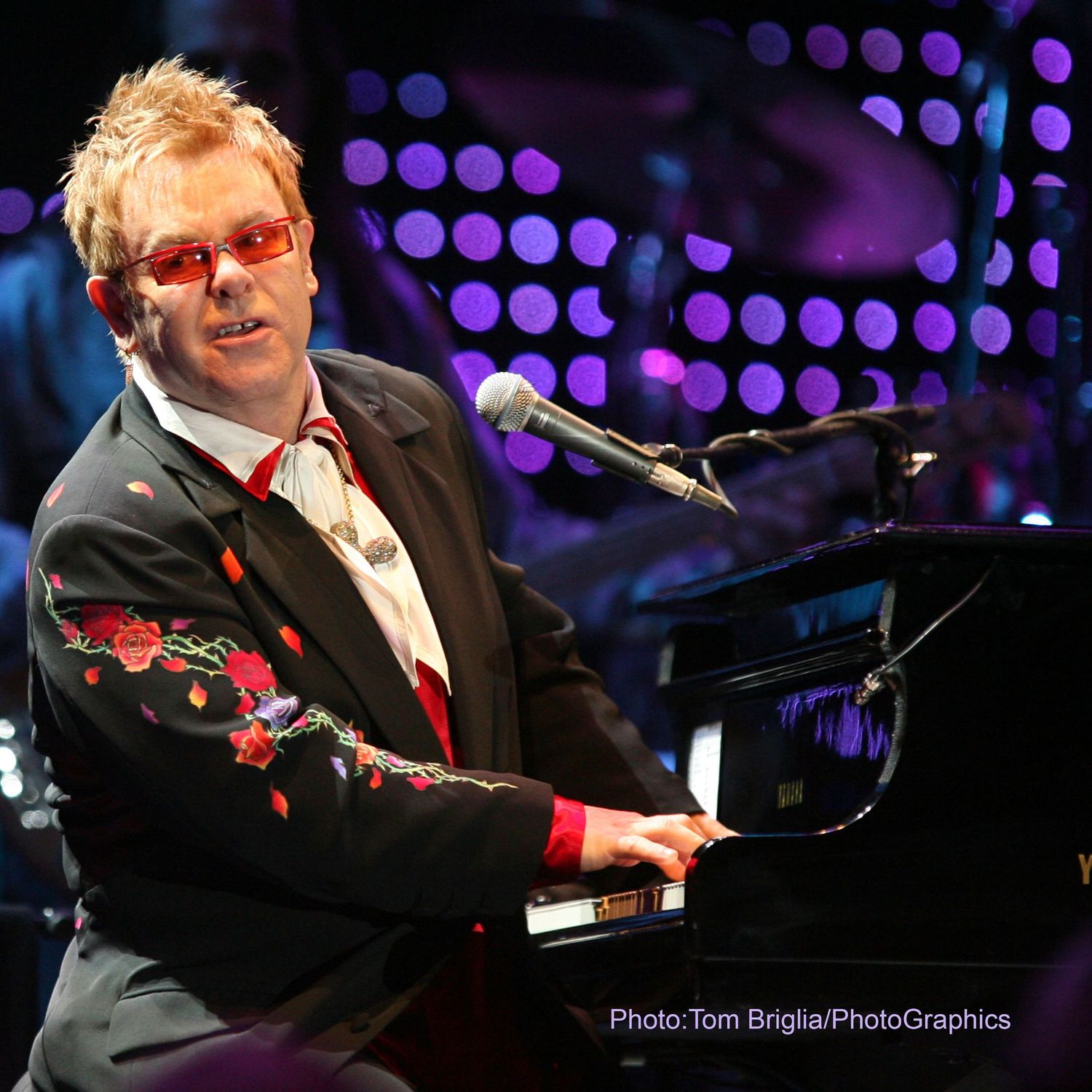 Musician performing at piano with purple spotlight effects in concert setting.