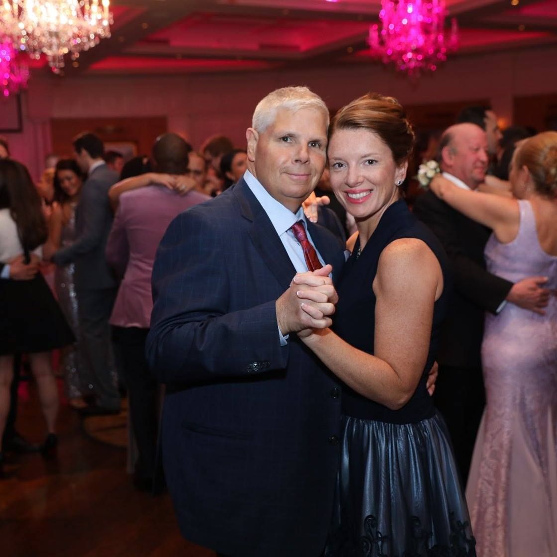 Couples dancing together at an elegant wedding reception with pink lighting and chandeliers.