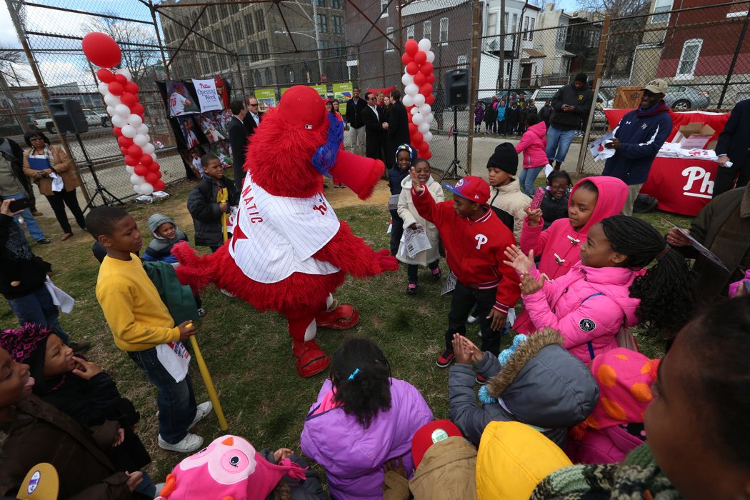 Crowd gathered at outdoor event with red and pink balloons and decorations.