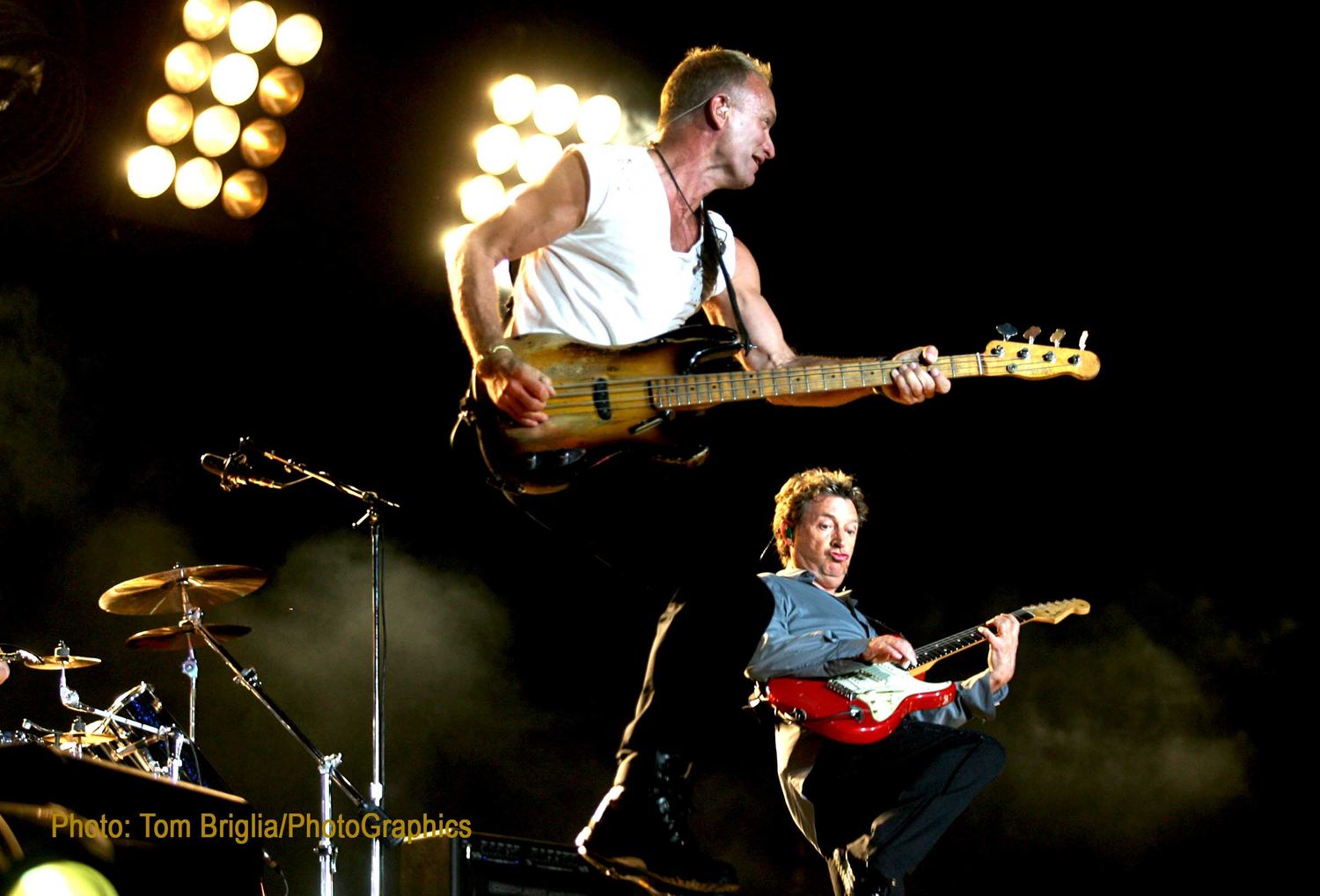 Two musicians performing energetically on stage with electric guitars under bright spotlights.