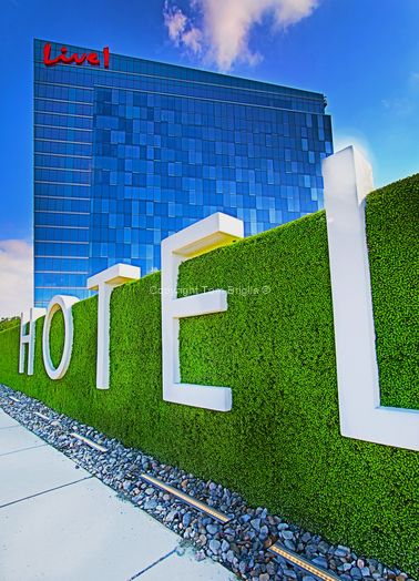 Modern hotel exterior with green hedge wall spelling out HOTEL against blue glass facade.