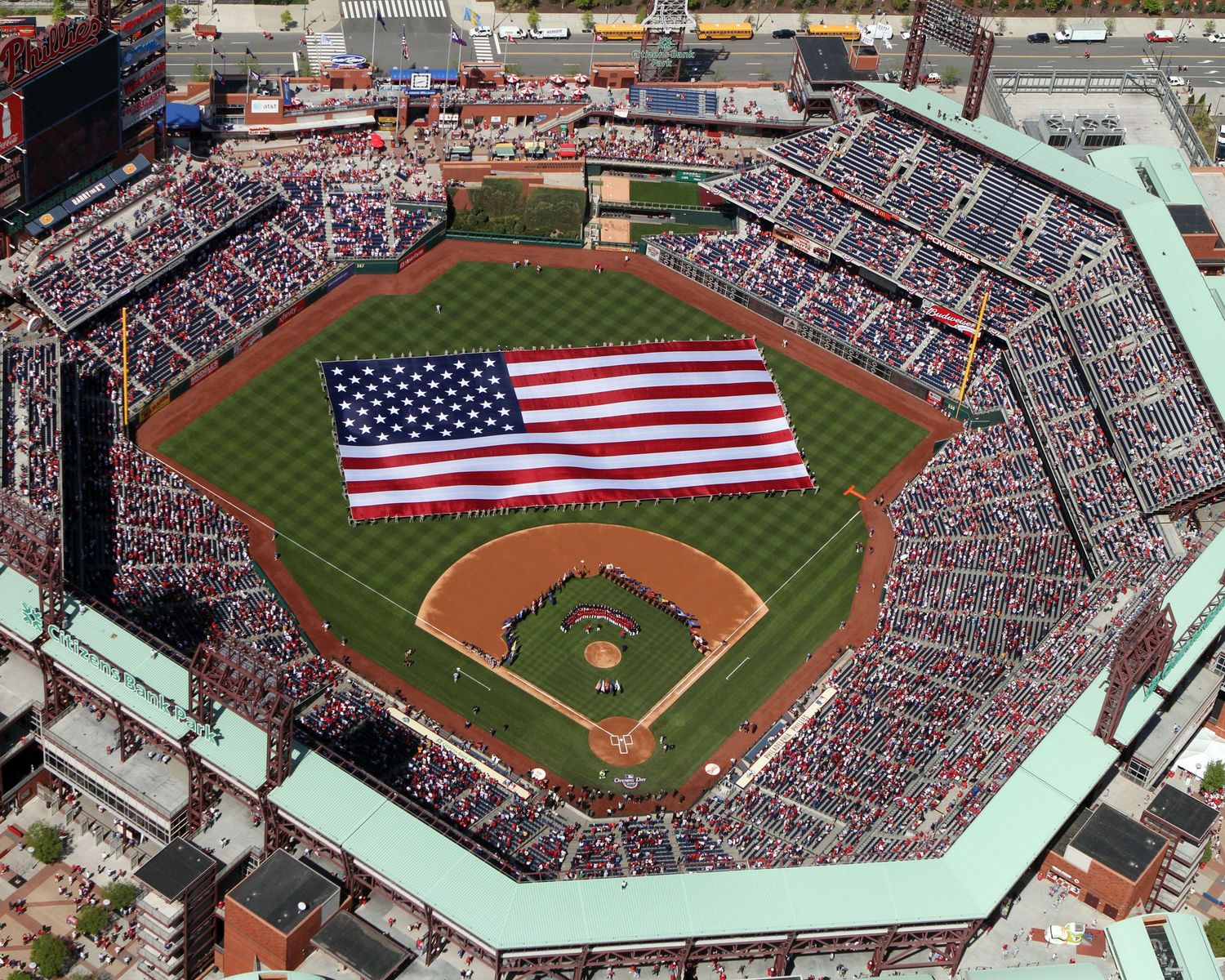 Baseball stadium filled with crowds and large American flags displayed on the field during special events.