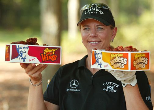 Staff members in black uniforms and caps holding fast food products outdoors.