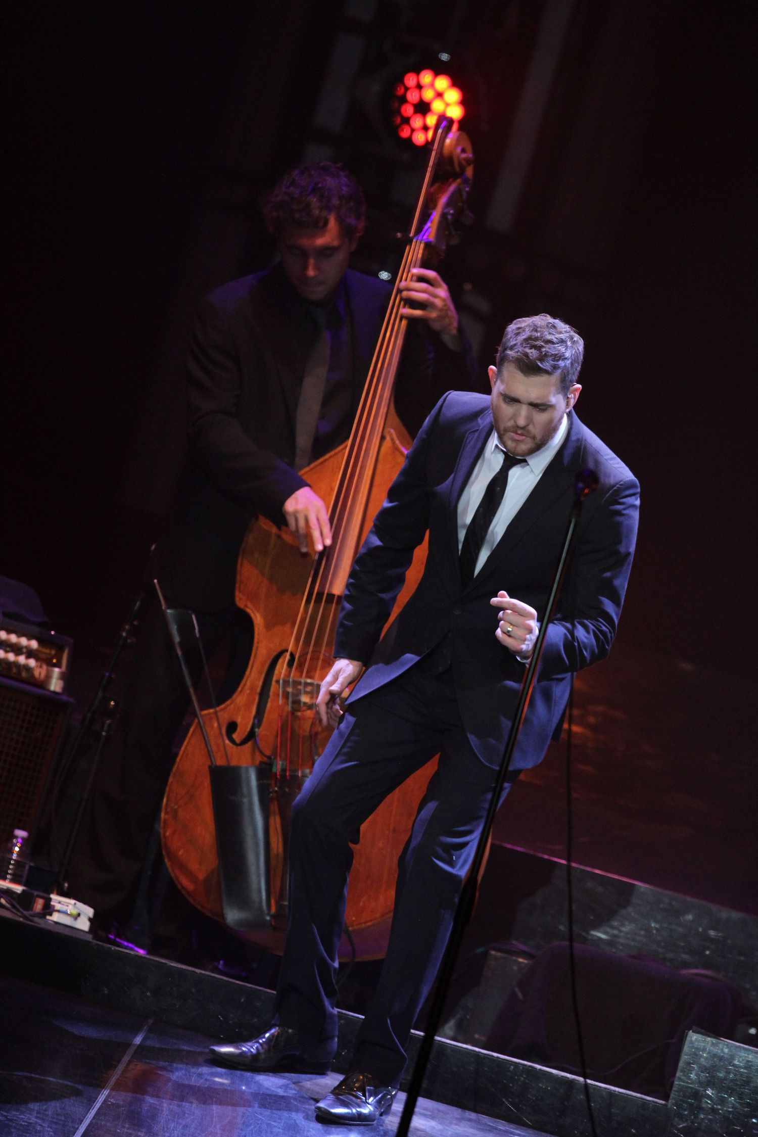 Jazz performers on dark stage with upright bass and microphone in formal attire.