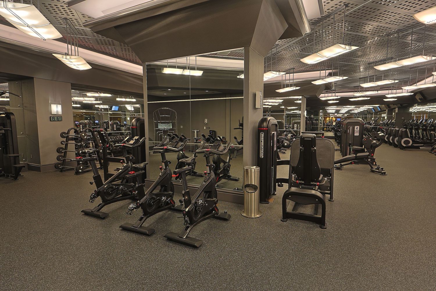 Large fitness center with rows of exercise equipment and machines under fluorescent lighting.