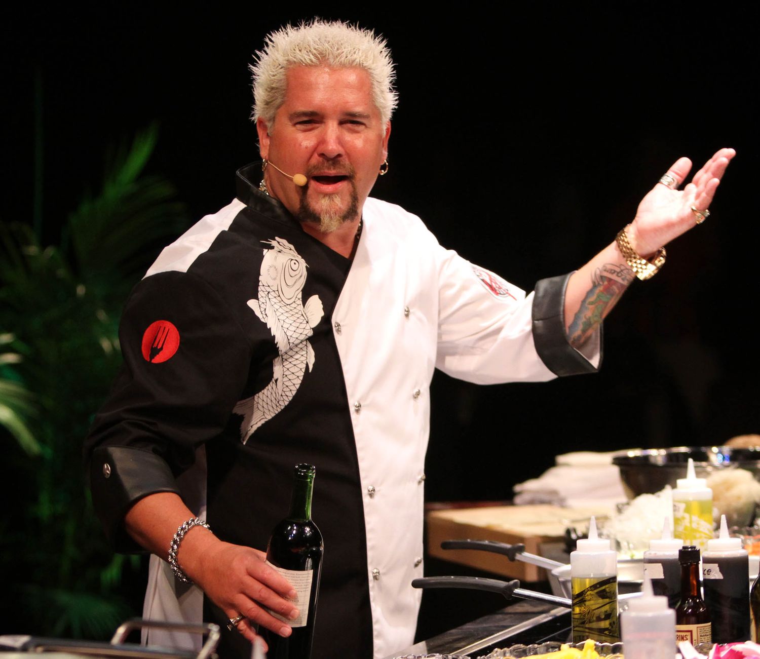 Chef in white coat demonstrating cooking techniques during a live presentation.