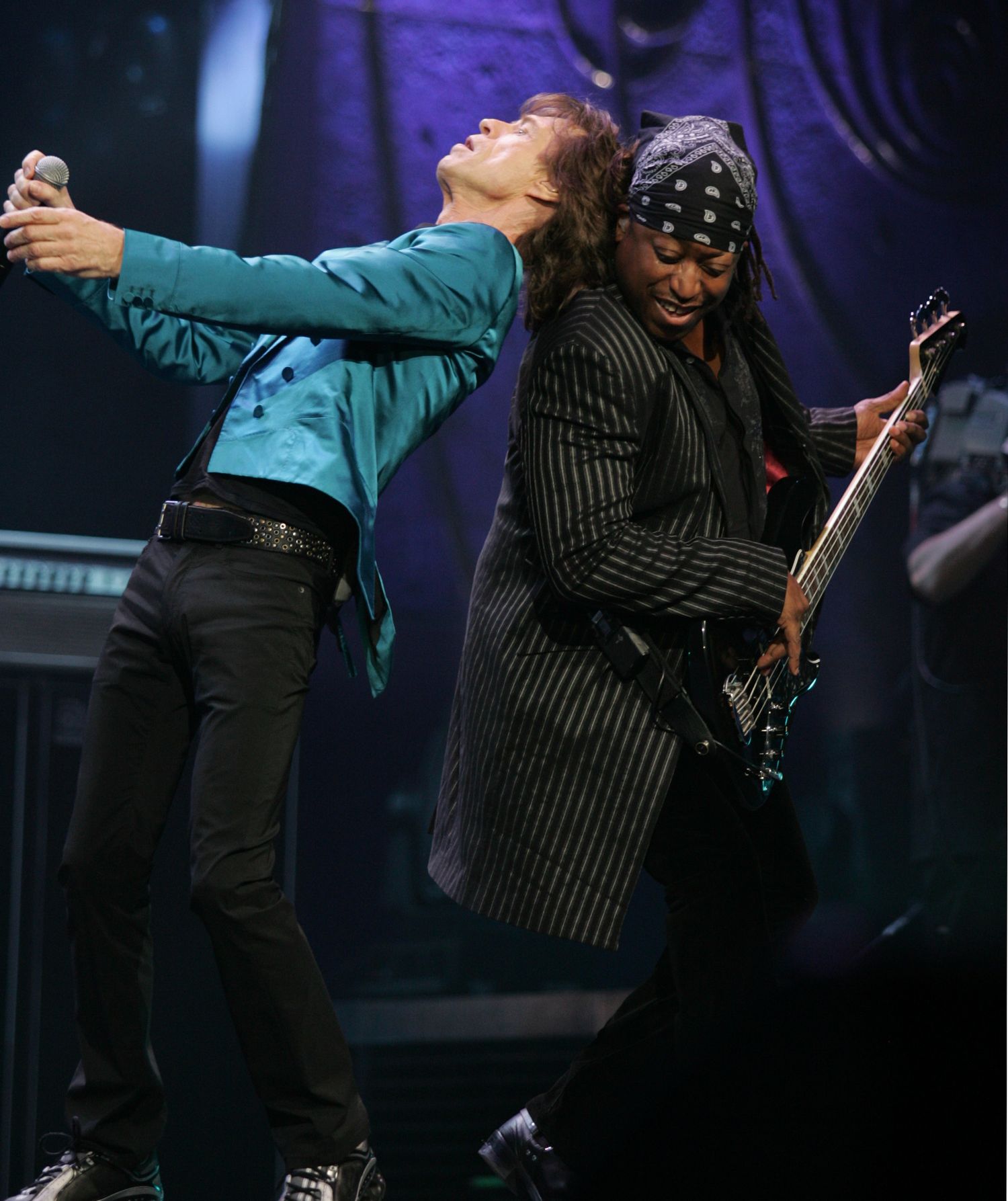 Two musicians performing together on stage with dramatic purple lighting.