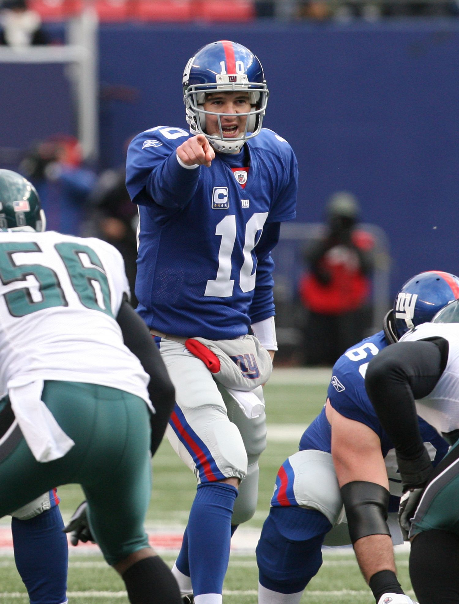 NFL quarterback in blue jersey calling signals at line of scrimmage against Eagles defense.