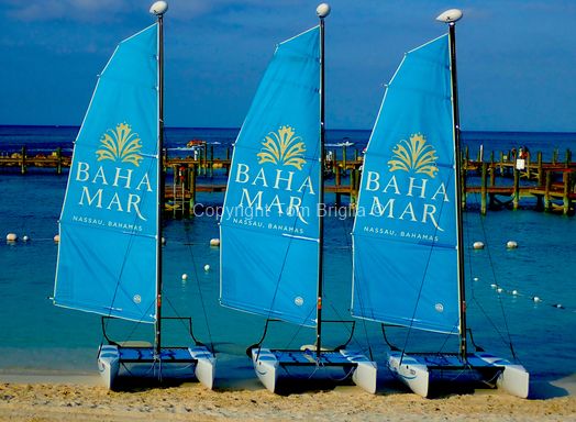 Line of blue sailboats with 'Baha Mar' logos lined up on a tropical beach.