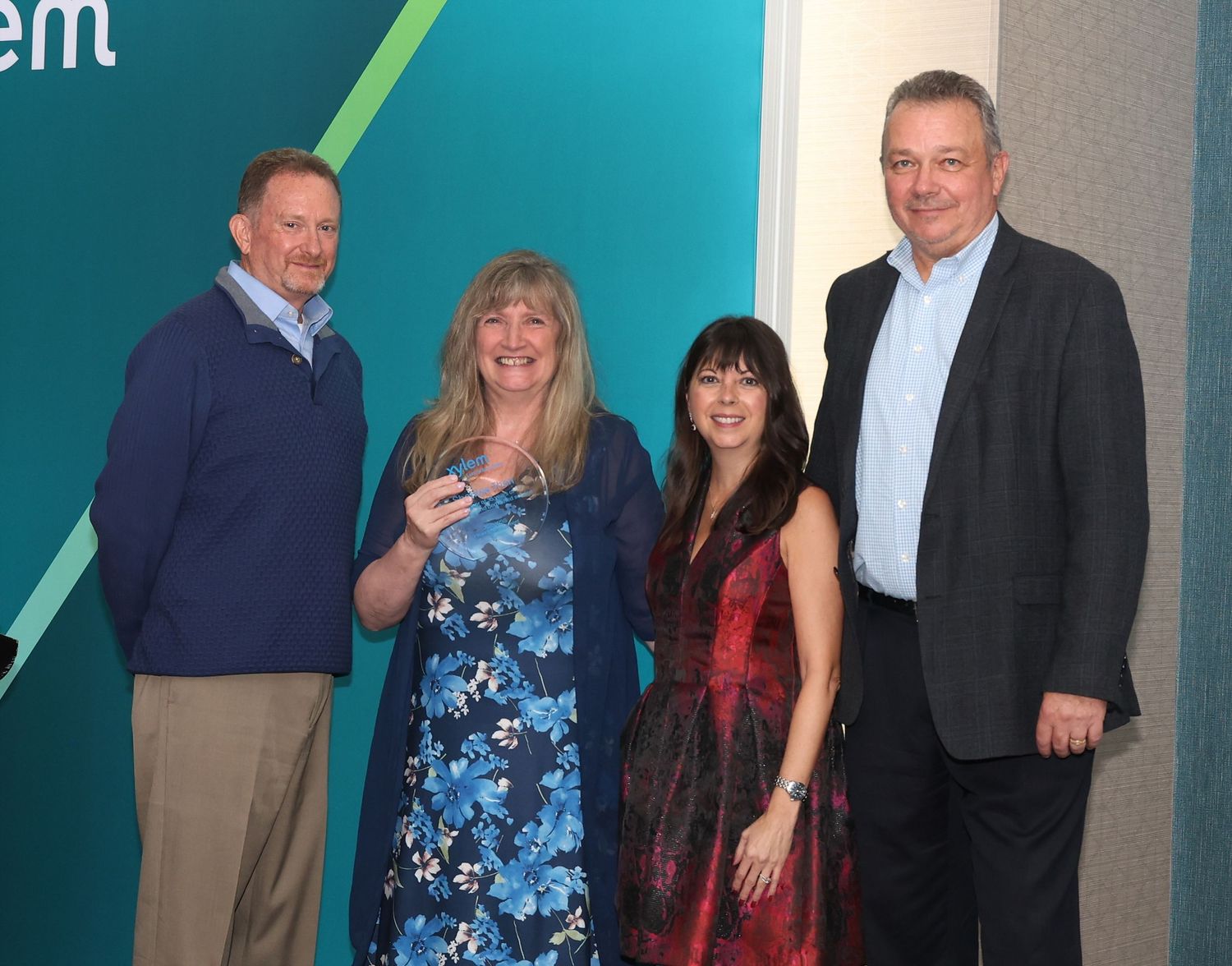 Four people pose together at a professional event, with two wearing business attire and two in more casual dress.