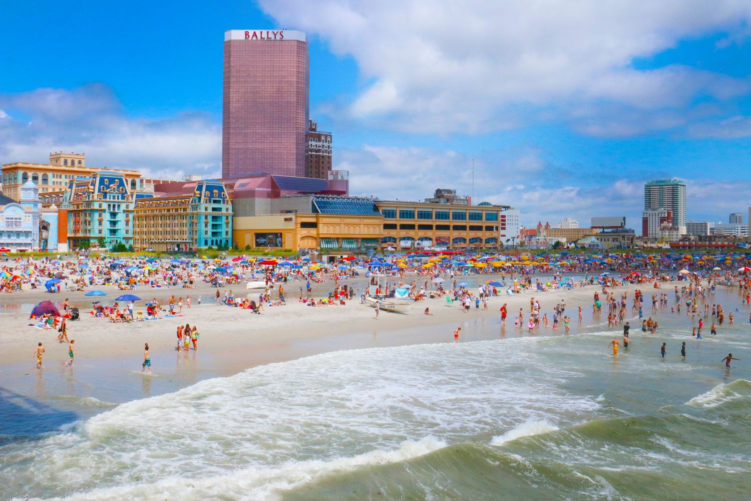 Aerial view of a crowded beach with colorful umbrellas and buildings along the shoreline.