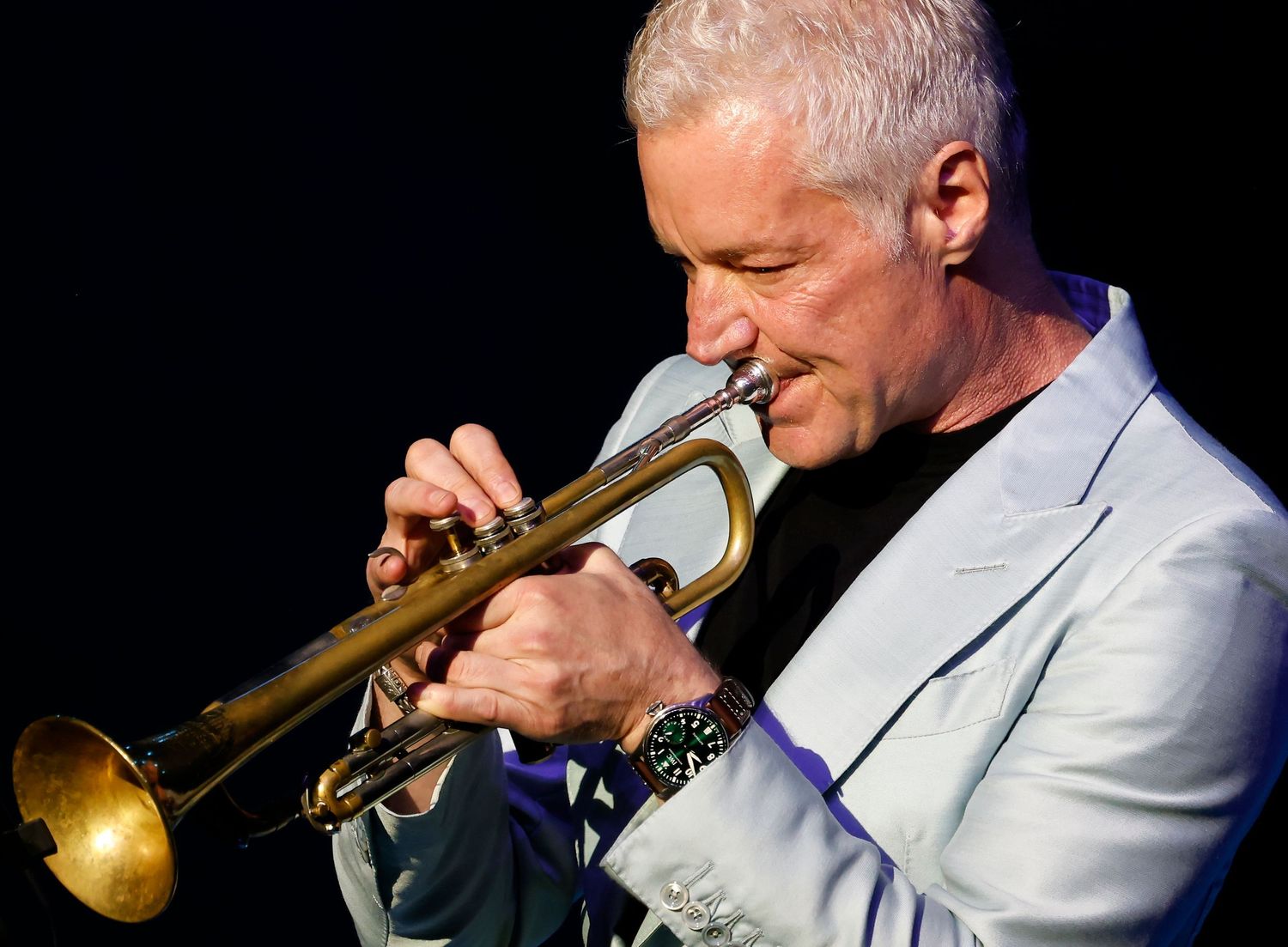Trumpet player performing on stage with dramatic black background and spotlights.