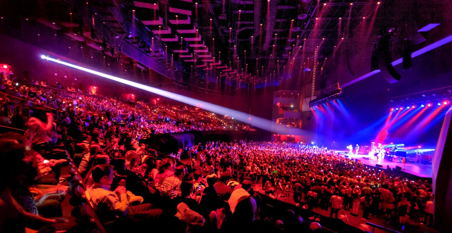 Concert venue illuminated with purple lighting and laser effects.