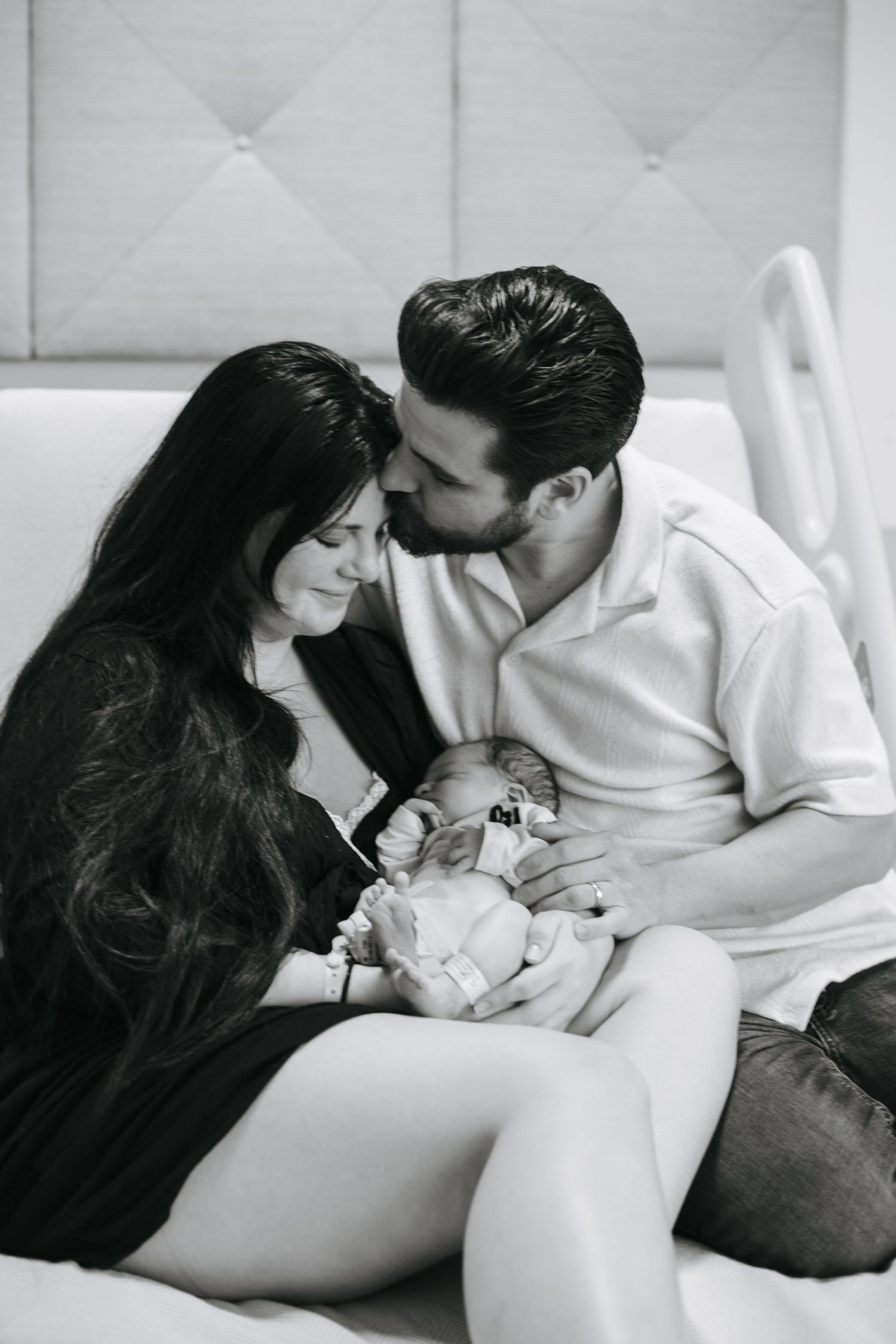 A black and white photograph capturing an intimate family moment in a medical setting.