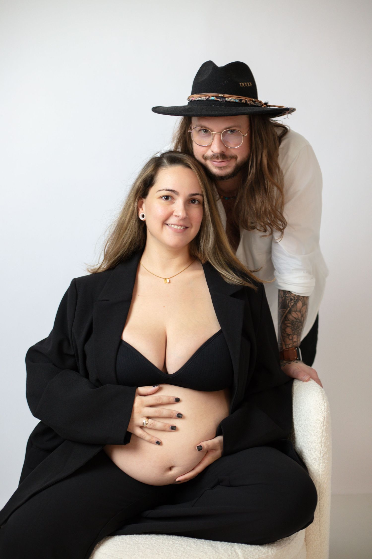 A maternity photo showing a couple in black attire posing together against a white background.
