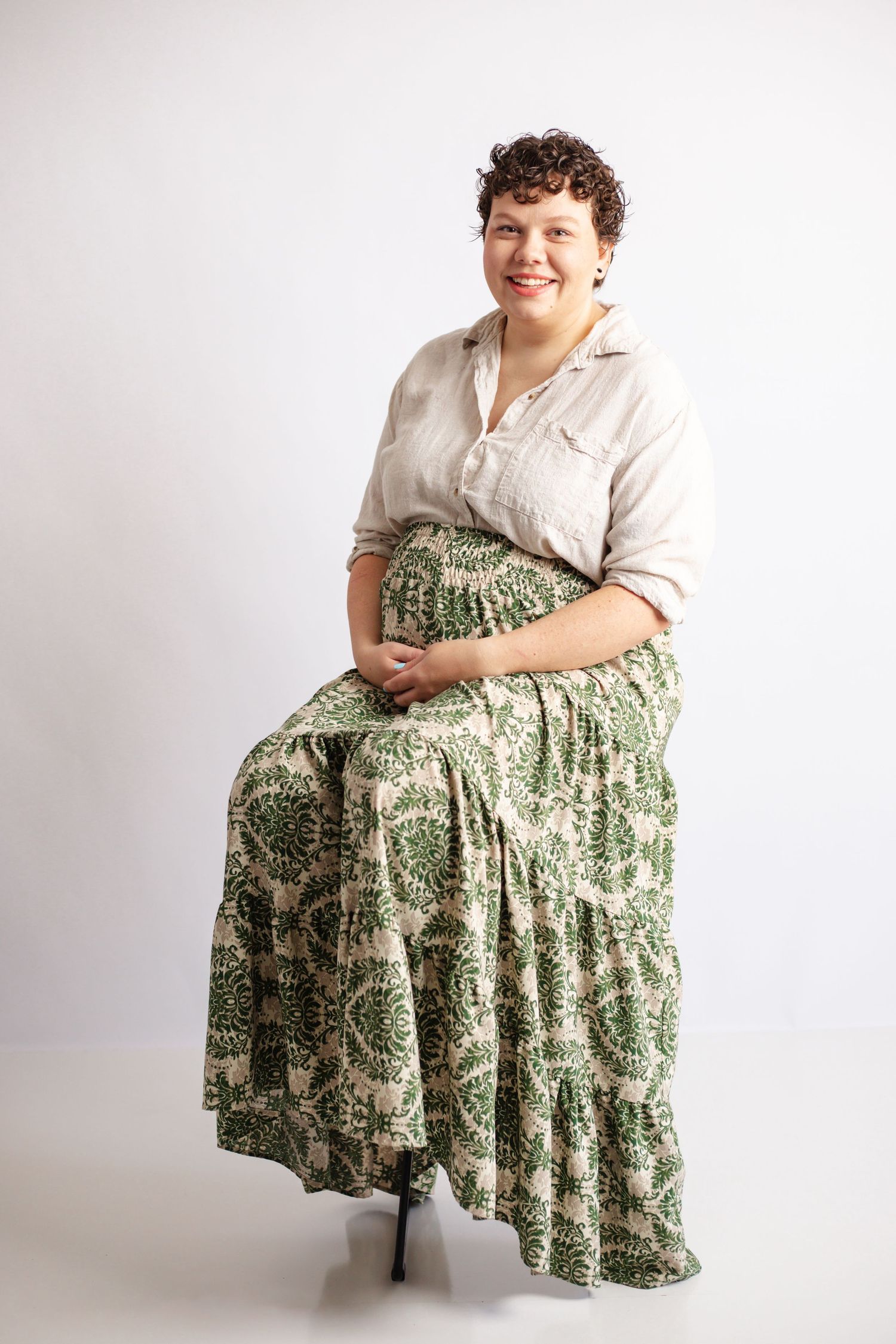 A person wearing a white blouse and green floral skirt poses in various seated positions against a white backdrop.
