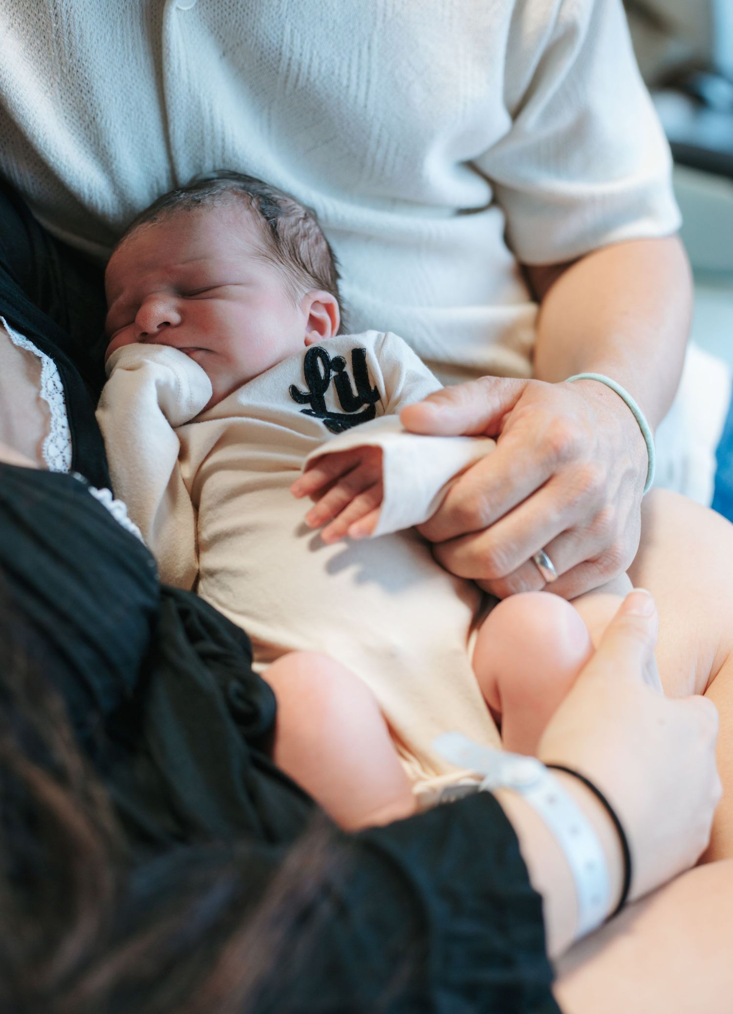A sleeping newborn baby in a white onesie rests peacefully on someone's lap.