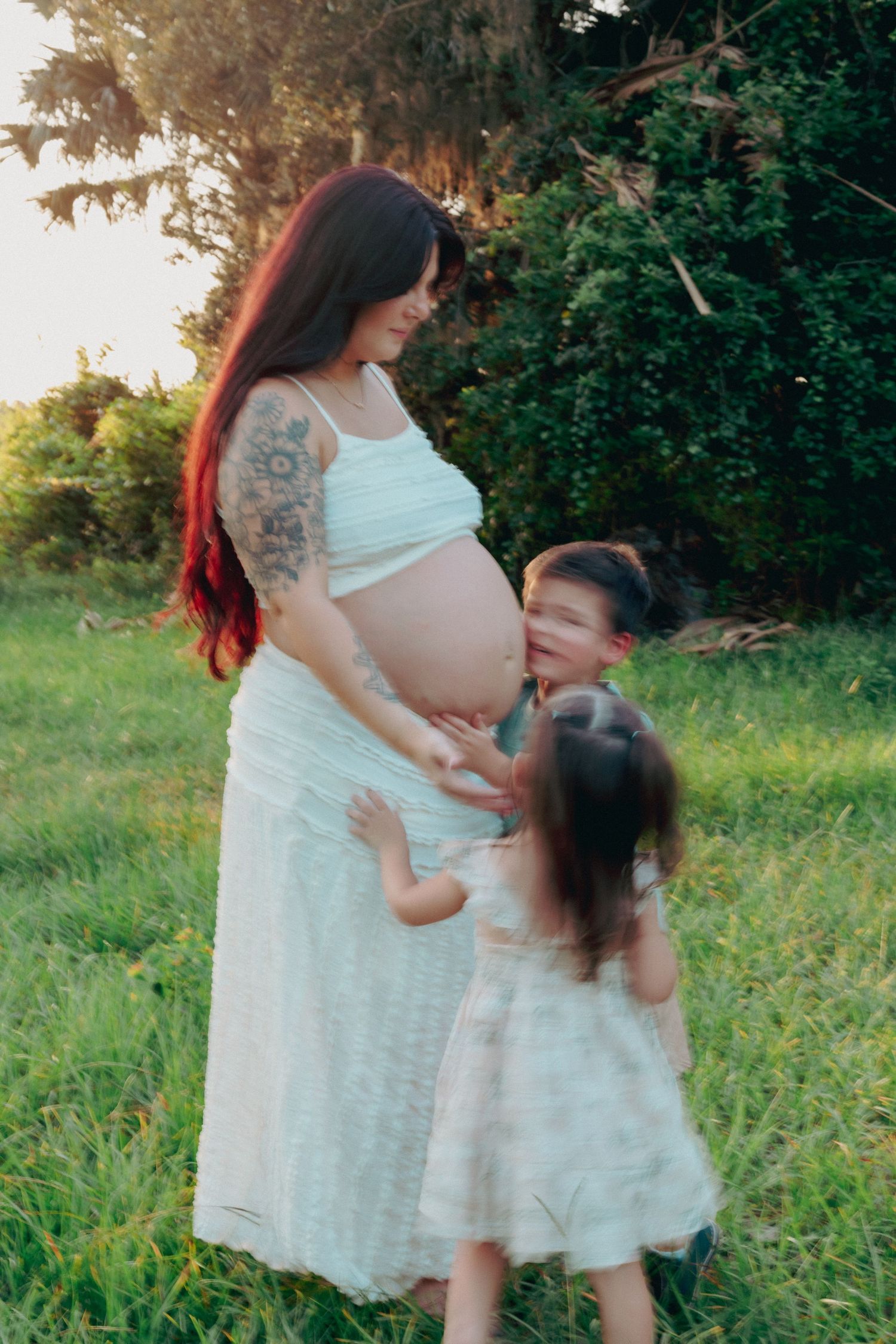 A maternity photo in a garden setting with children touching a pregnant belly.