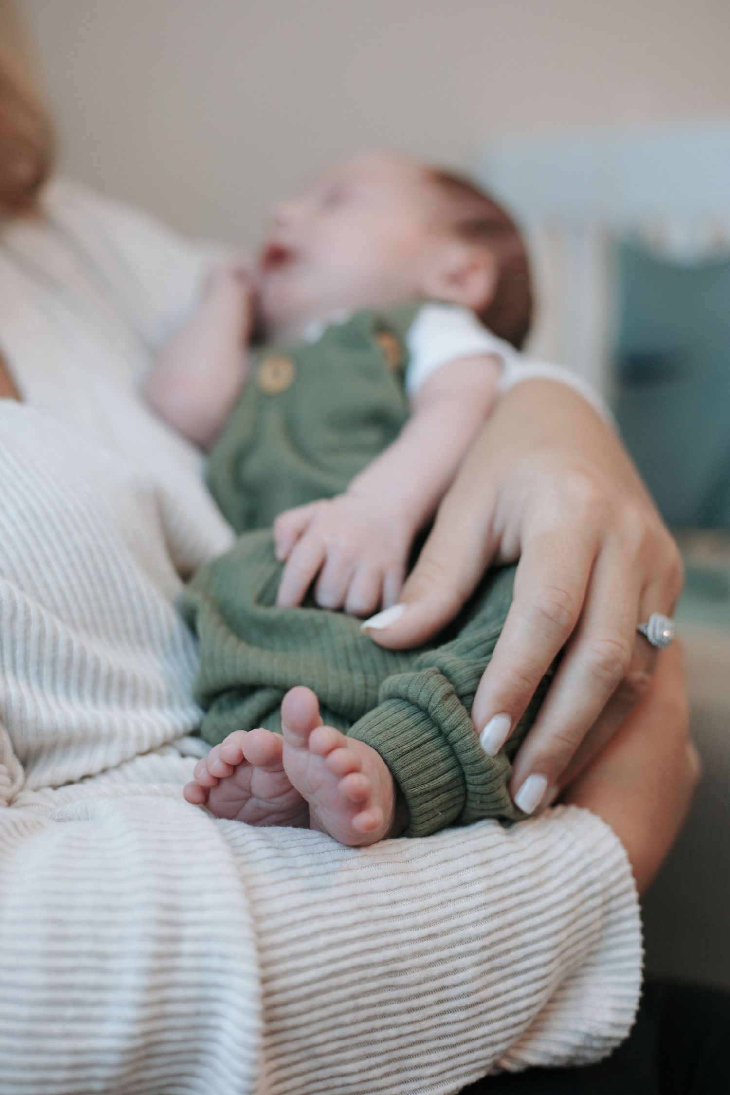 Close-up of small baby feet and hands with adult fingers against a textured white blanket.