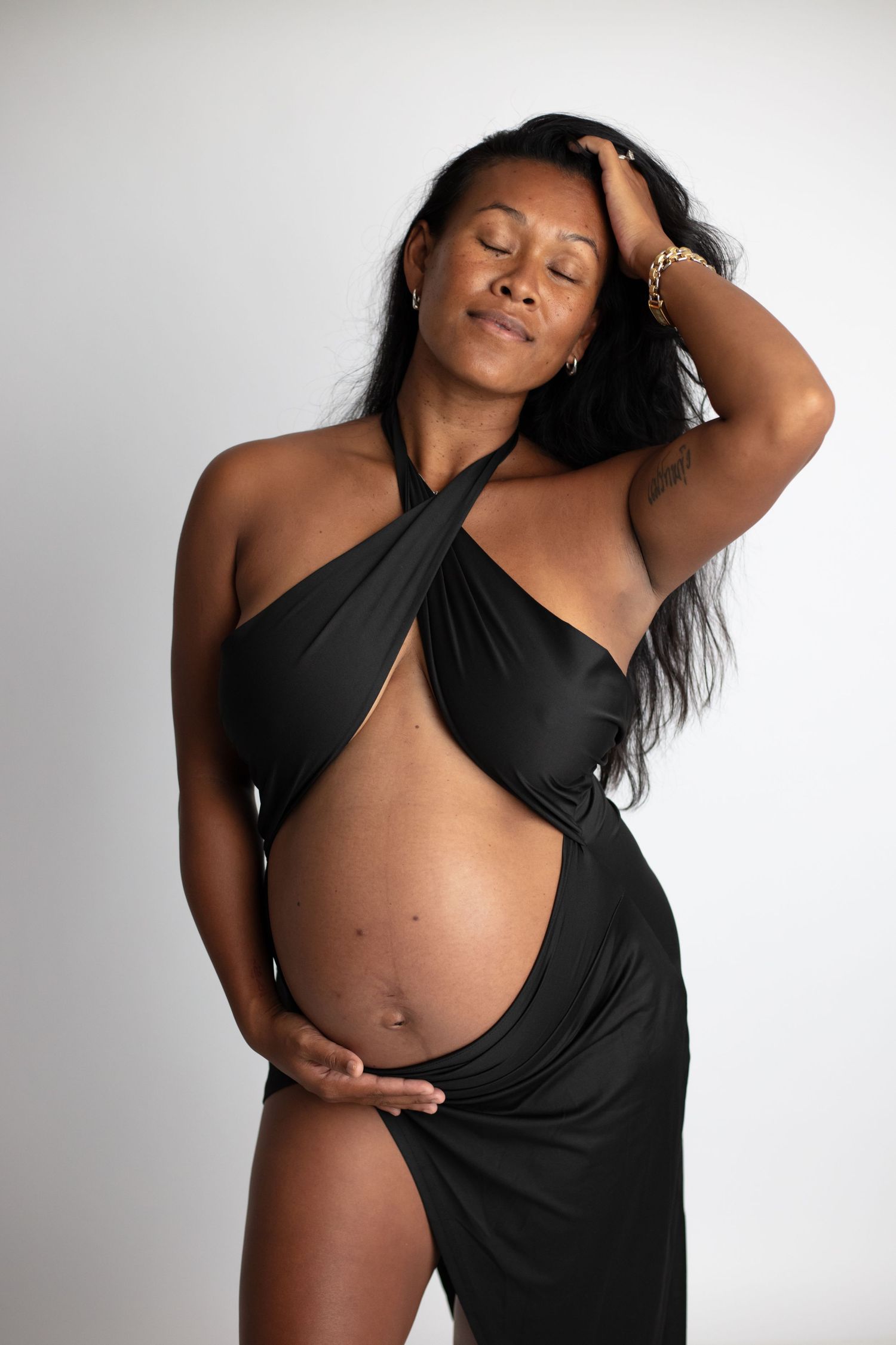 Minimalist maternity boudoir series featuring black asymmetrical wrap against white background.