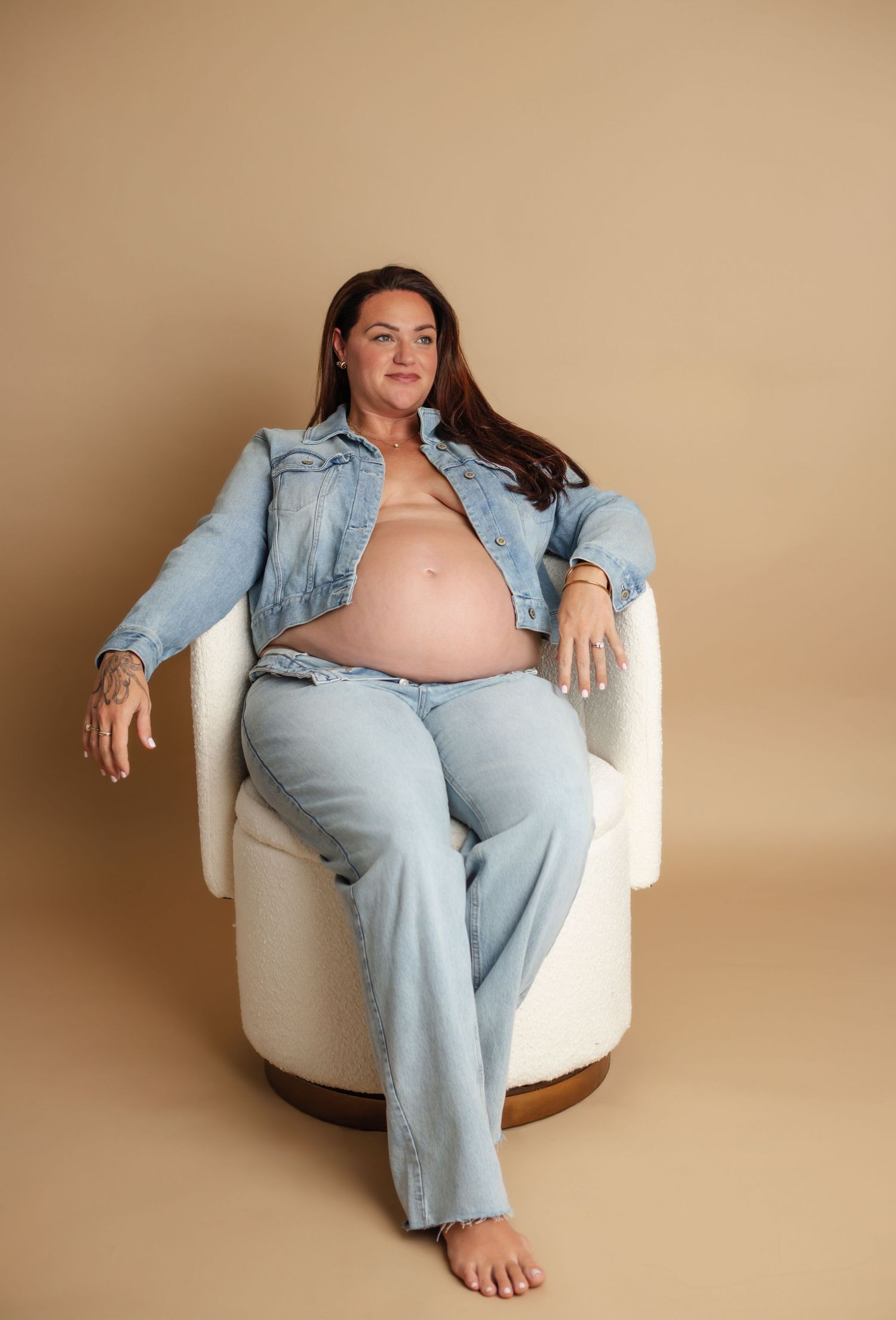 A series of maternity photos showing a pregnant person in denim clothing lounging casually in a white chair against beige backdrop.