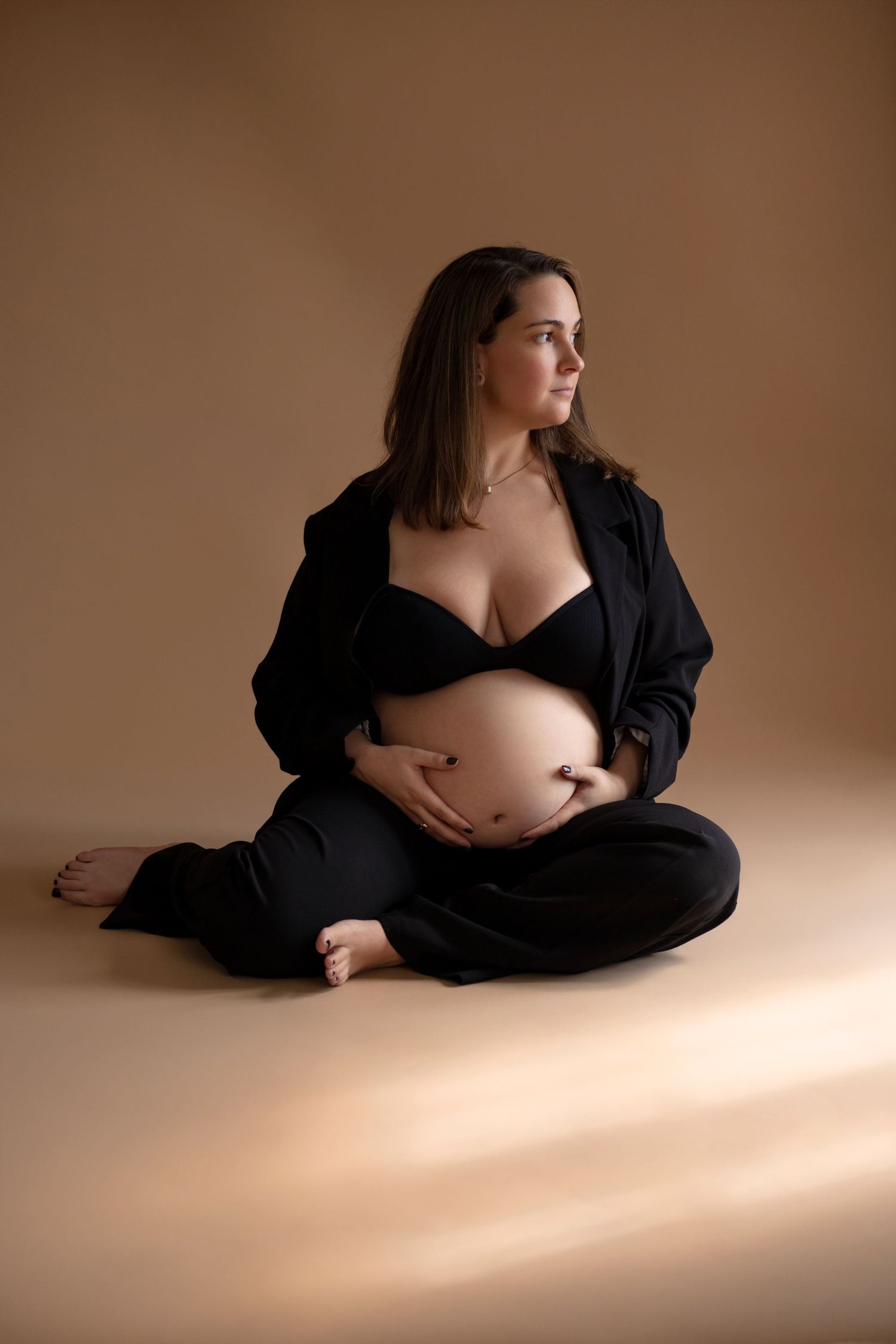 Artistic maternity boudoir photo series in black against warm brown backdrop with dramatic lighting.