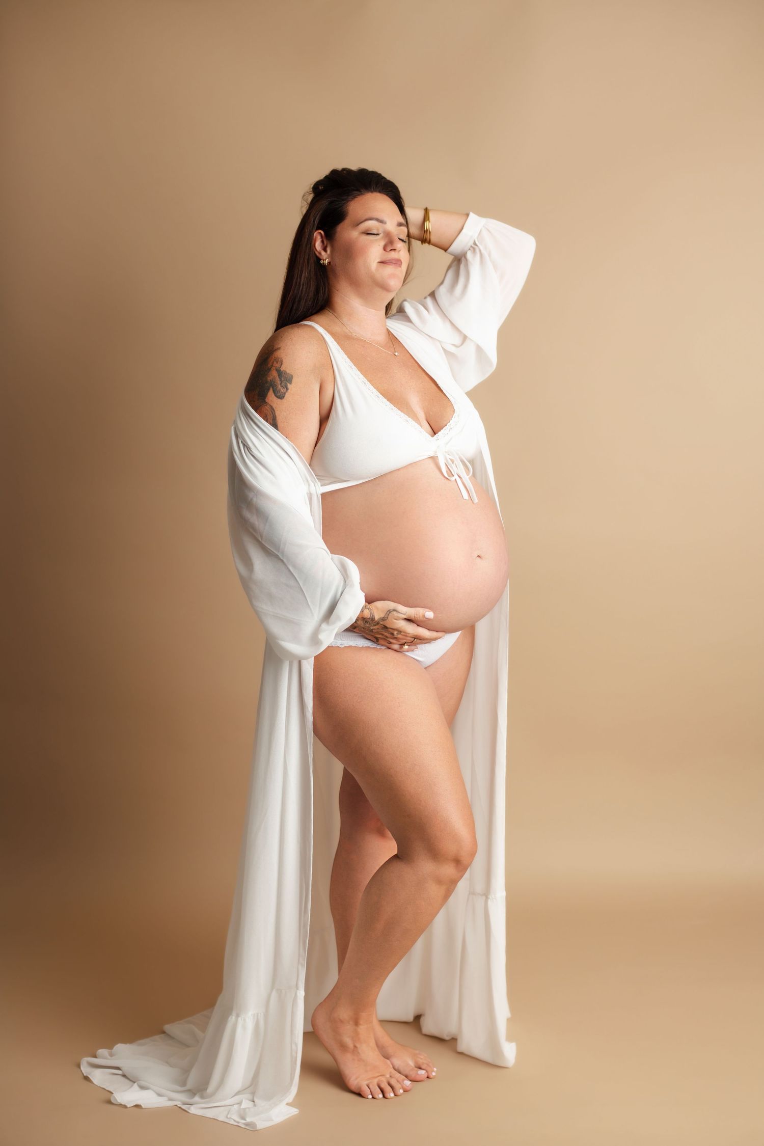 Graceful maternity portraits in peach bodysuit and white robe against neutral backdrop.