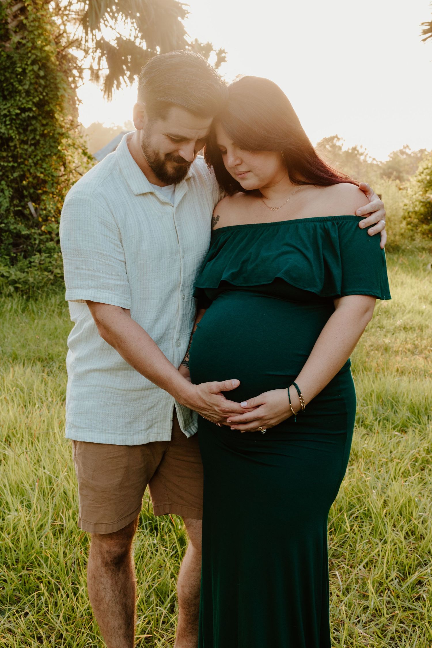 A maternity photo of a couple embracing outdoors, with the woman wearing an emerald green dress.