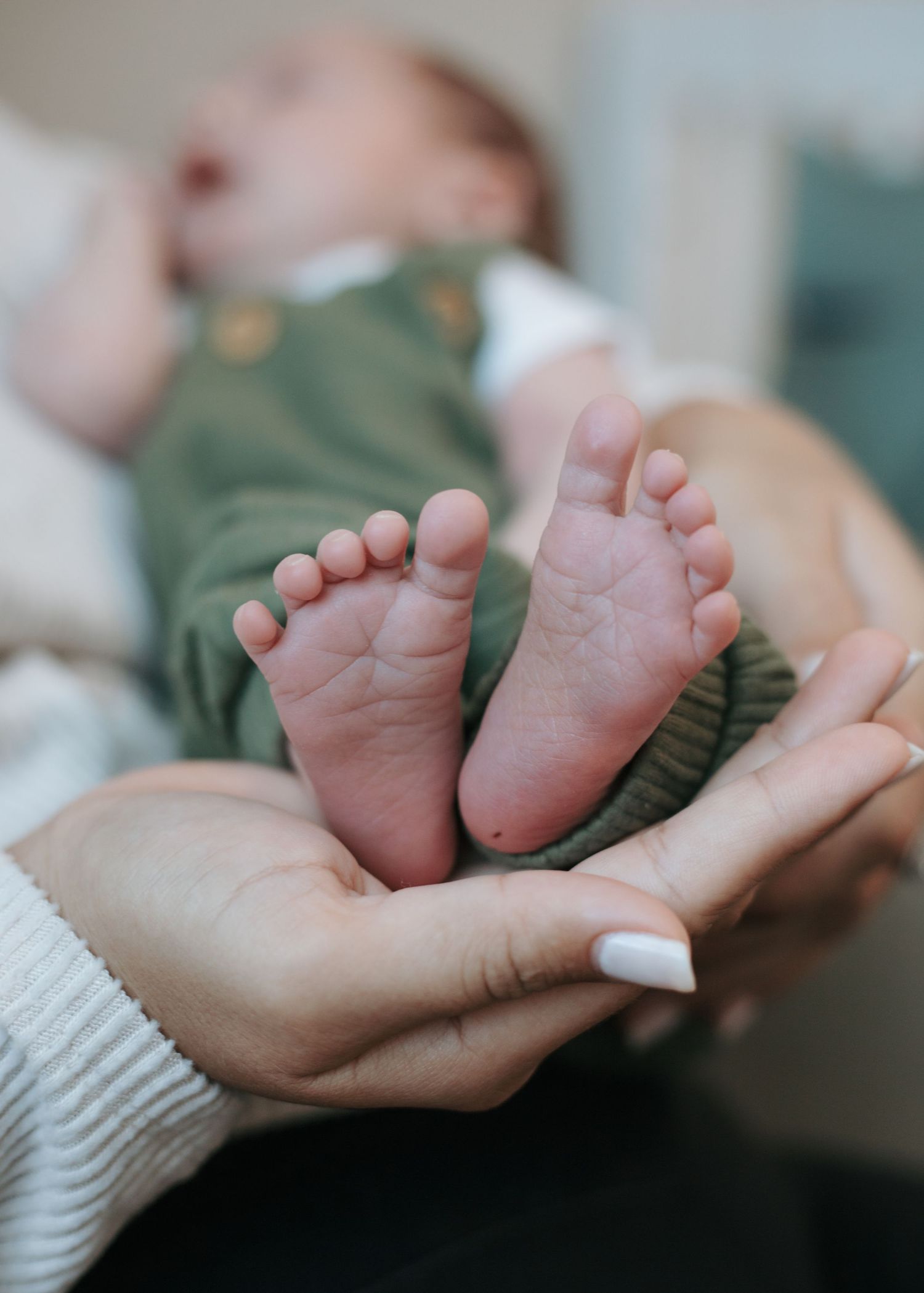 Tender close-up series of tiny newborn baby feet being gently cradled in adult hands wearing white knit sleeves.
