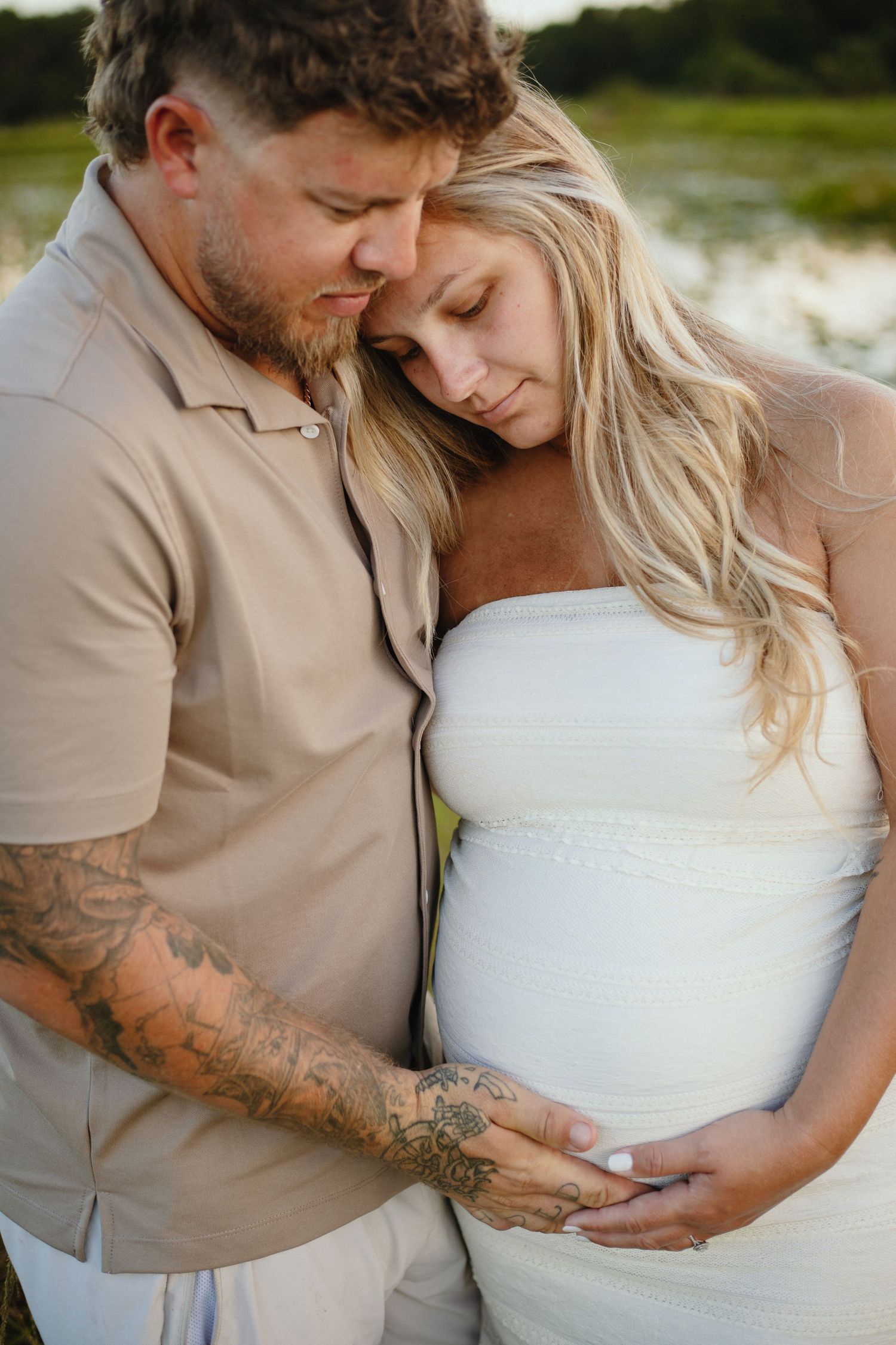 Outdoor maternity photoshoot featuring couple in beige and white outfits embracing.