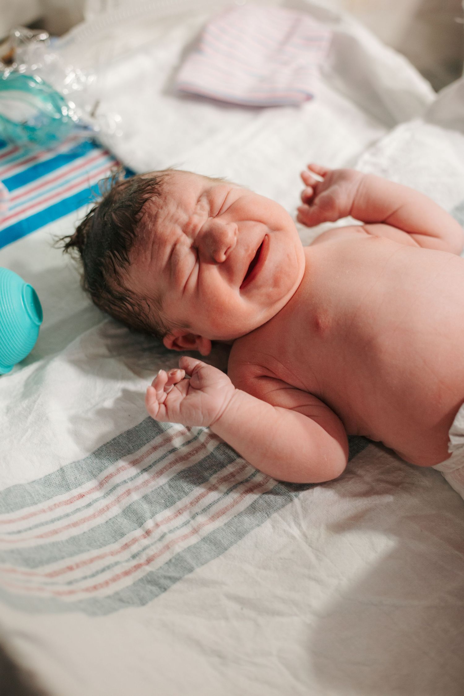 A newborn baby crying on hospital bedding surrounded by medical supplies.
