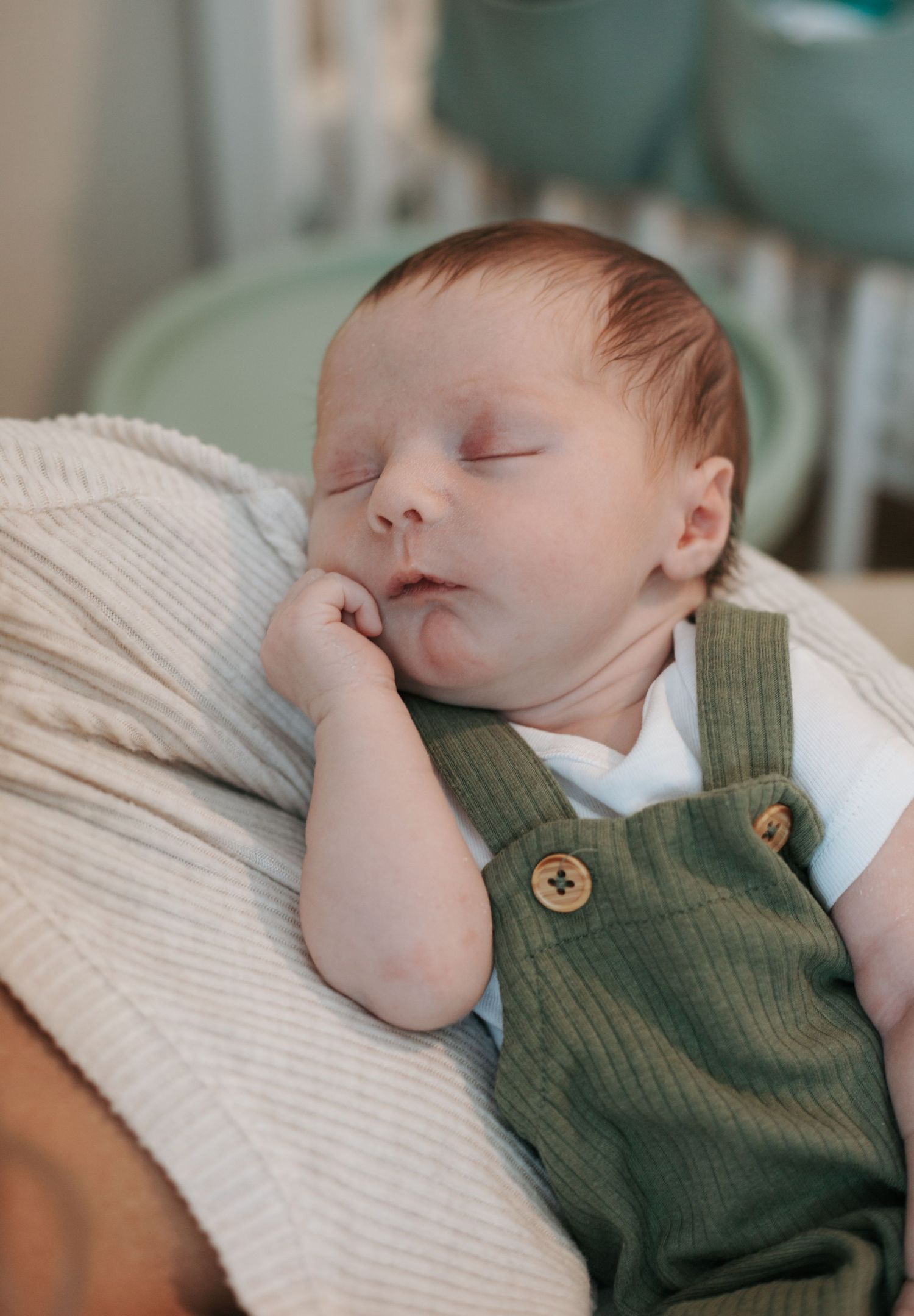 A sleeping baby wearing a green knit vest with wooden buttons rests peacefully.