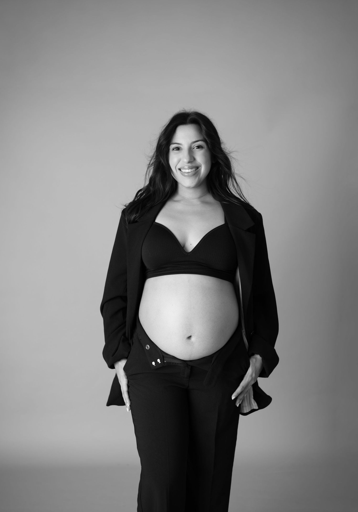 Black and white maternity photo series showing progression of pregnancy in elegant black blazer and dress.