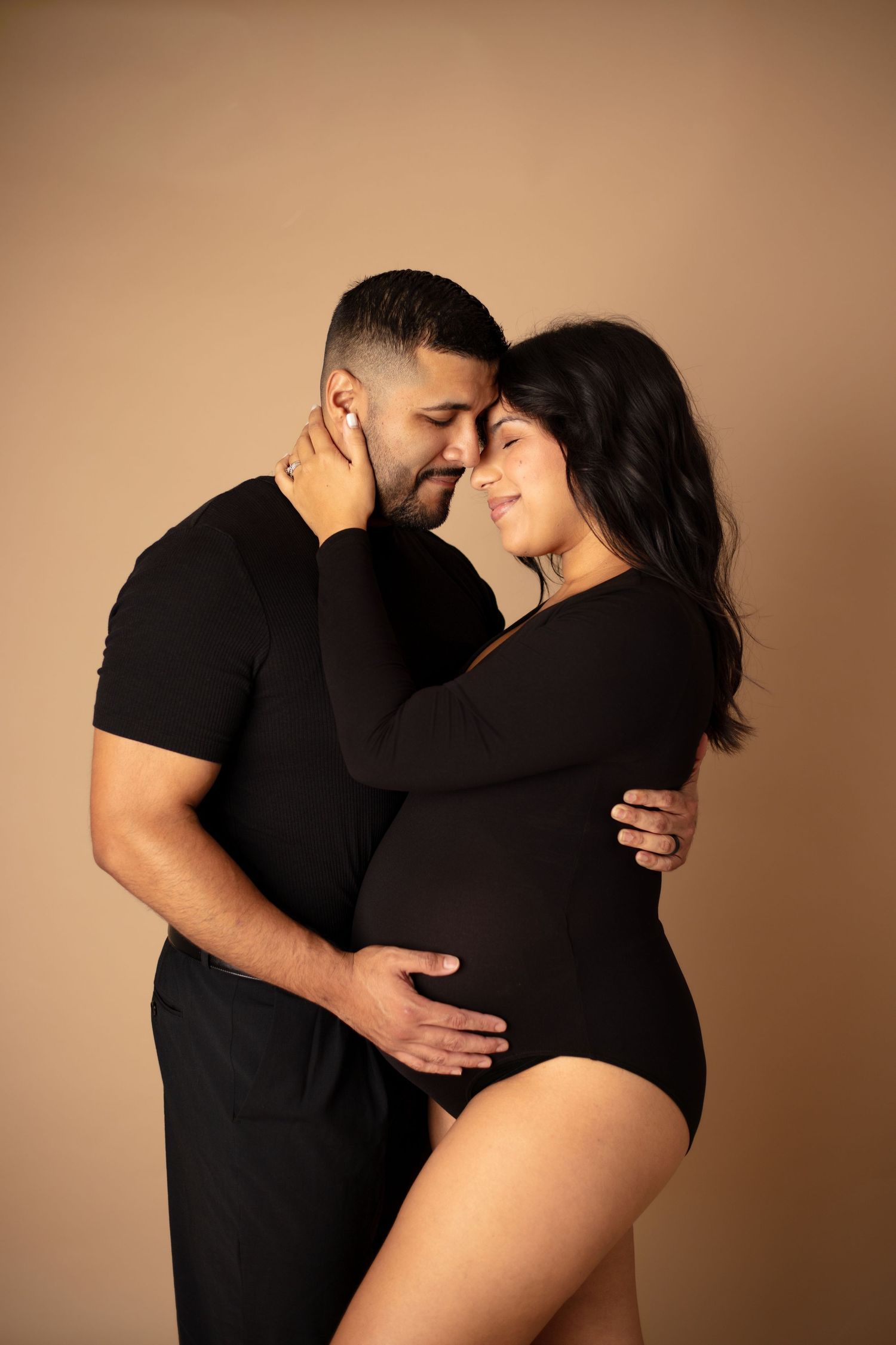 A romantic maternity photoshoot sequence showing a couple in black clothing embracing against a warm brown backdrop.