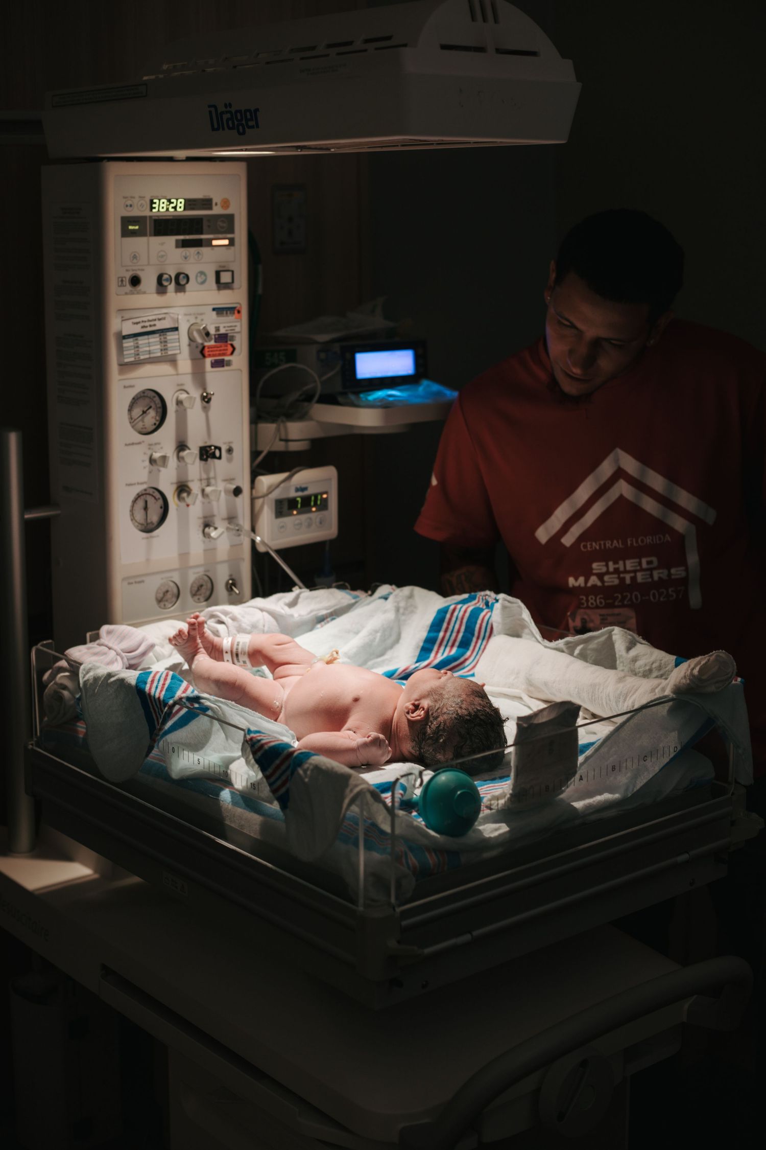 Medical equipment and monitoring devices surround a newborn in a dimly lit hospital nursery.