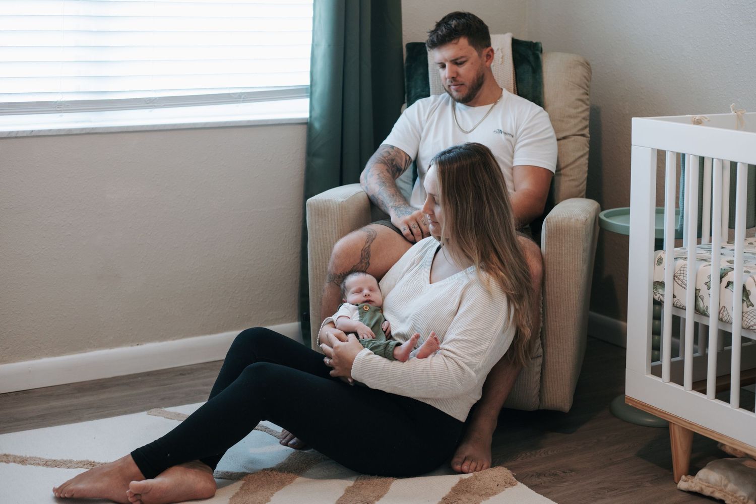 Family gathering in a nursery room with white furniture and green curtains.