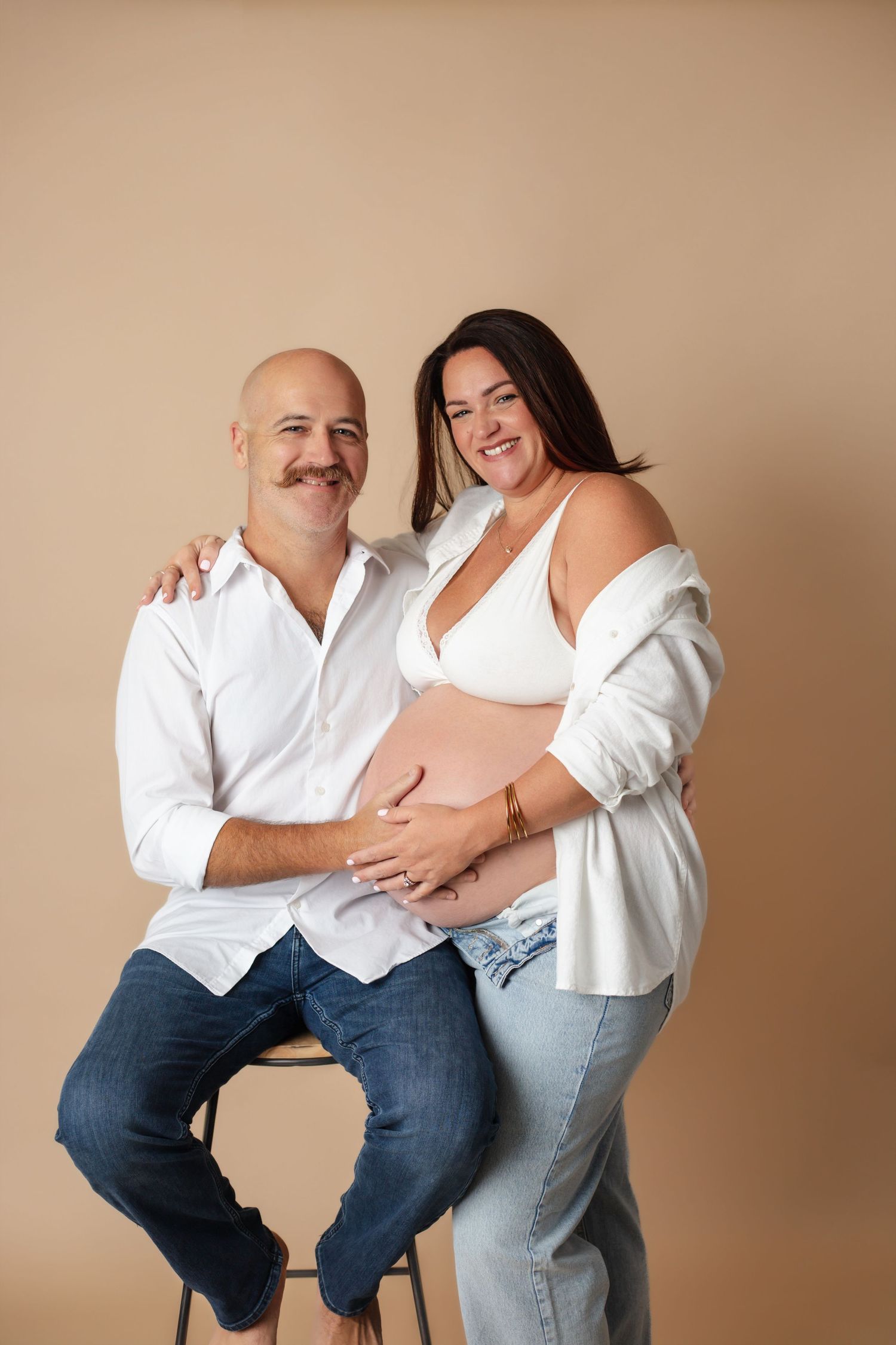 Casual studio maternity session with couple in white shirts and jeans.