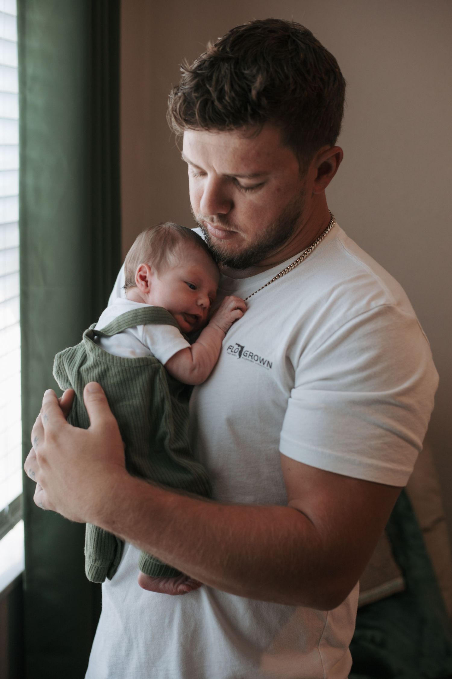 A gentle embrace while holding a sleeping infant wearing green clothing.